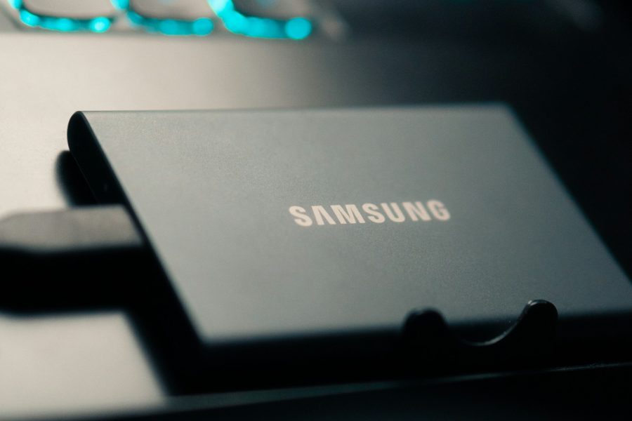 Samsung portable SSD connected beside a keyboard glowing blue, illustrating local photo storage for an online backup workflow