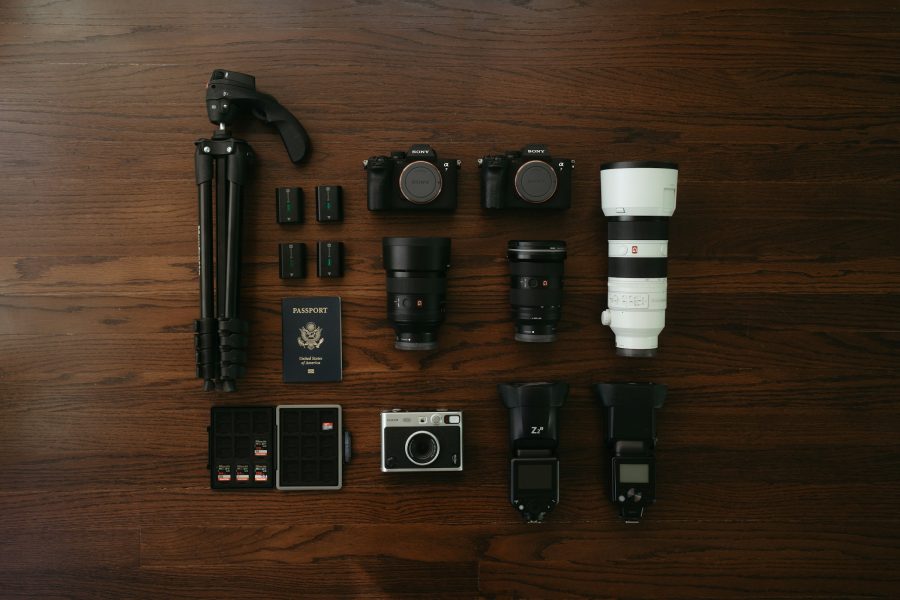 Flat lay of two mirrorless camera bodies, lenses, a tripod, batteries and memory cards on a wooden floor