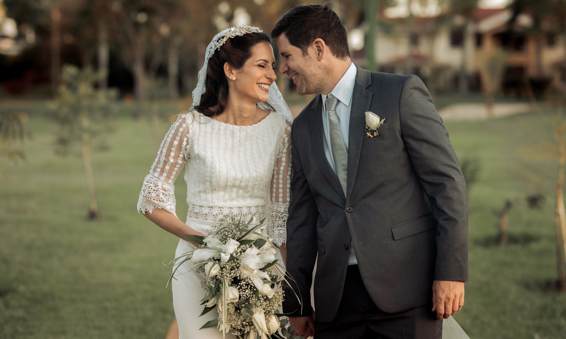 Bride and groom smiling together outdoors with a white bouquet during a wedding portrait
