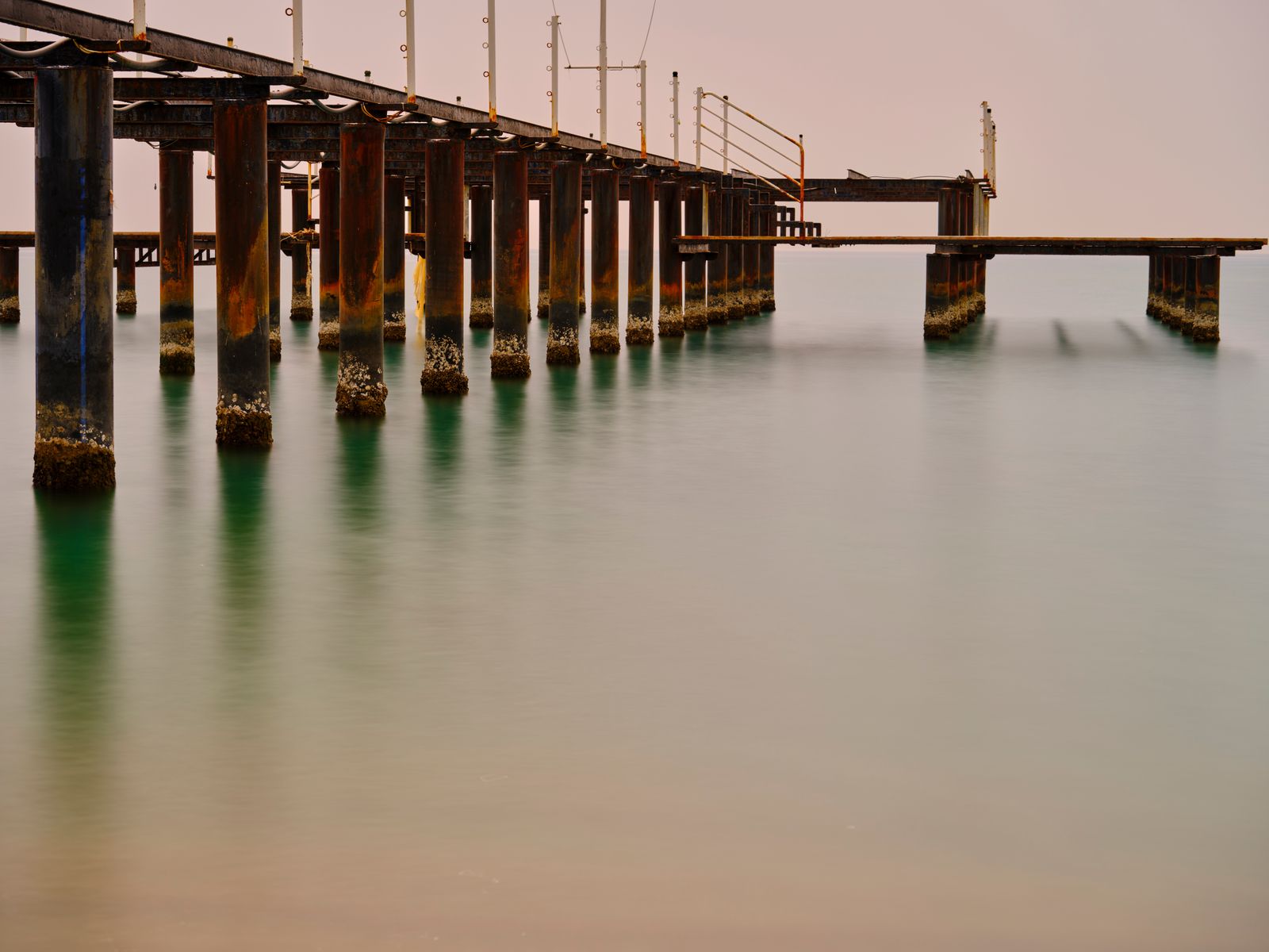 Long exposure of an old wooden pier over perfectly smooth sea with soft pastel sky and green reflections