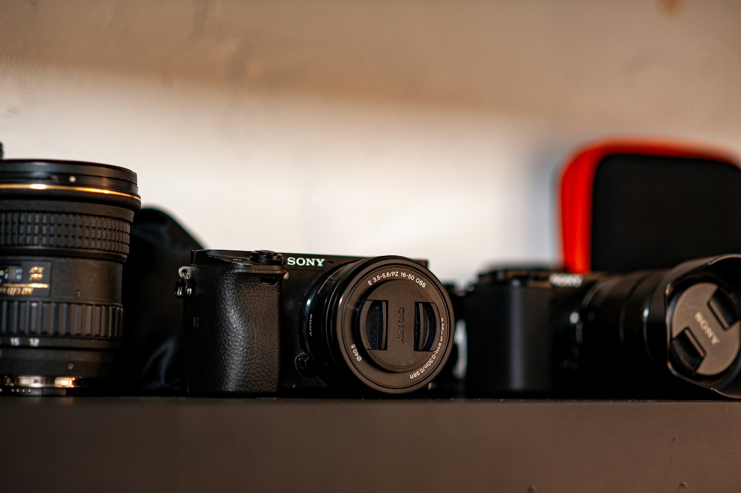 Two mirrorless camera bodies and several lenses lined up on a dark shelf