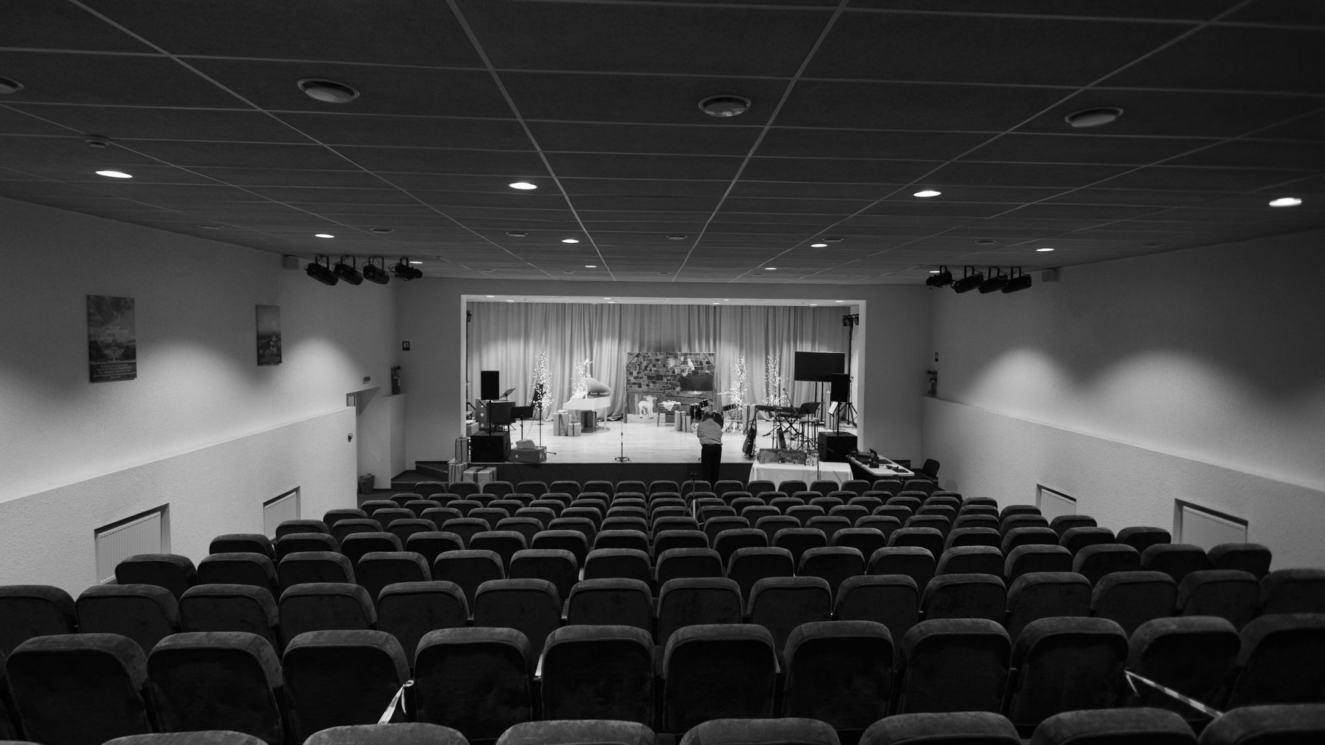 A black and white view of an empty auditorium with rows of seats facing a small stage