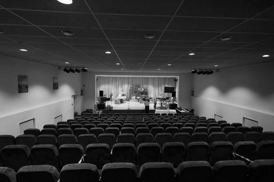 A black and white view of an empty auditorium with rows of seats facing a small stage