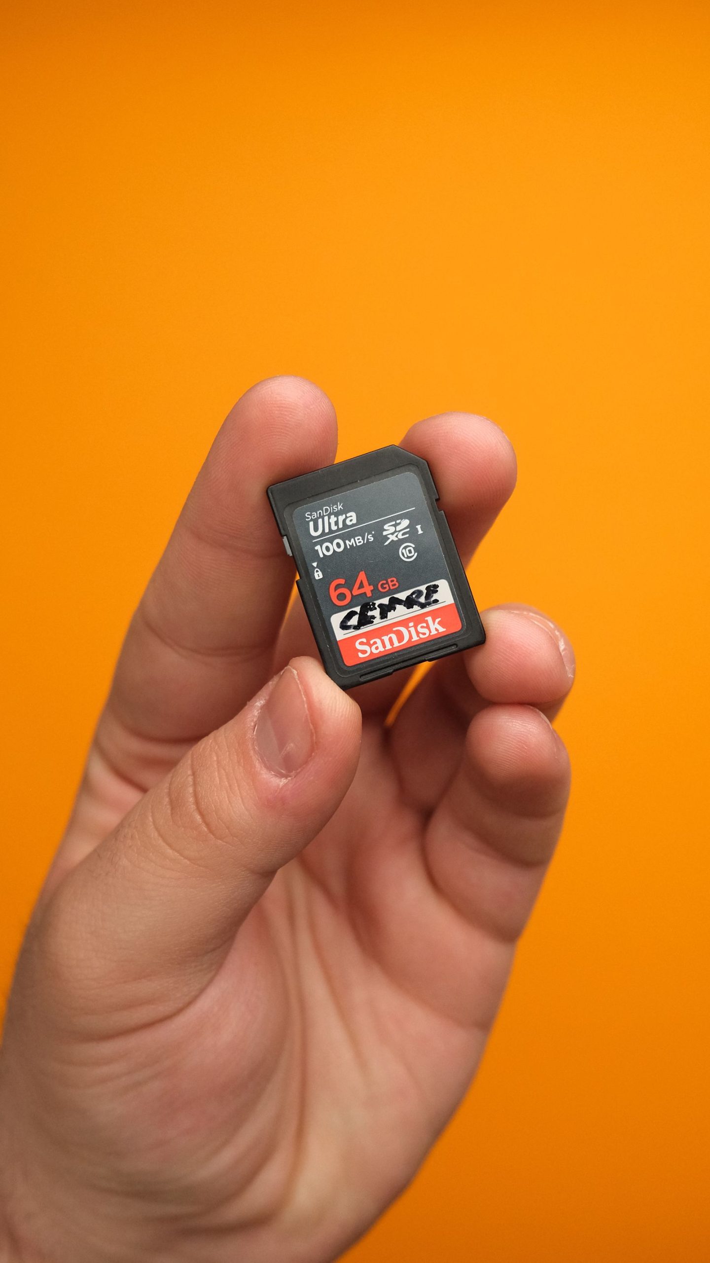 Hand holding an SD card on an orange background