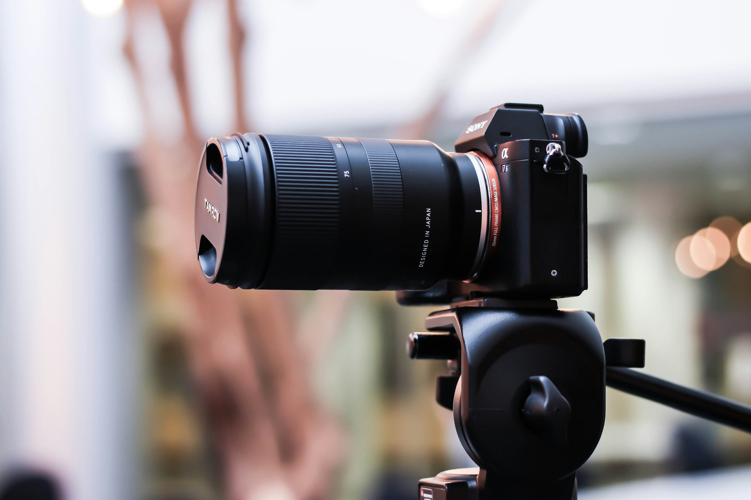 A mirrorless camera with a zoom lens mounted on a tripod head with a softly blurred room behind it