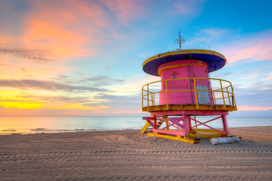 Pink and yellow Miami Beach lifeguard tower standing on the sand under a pastel sunrise sky