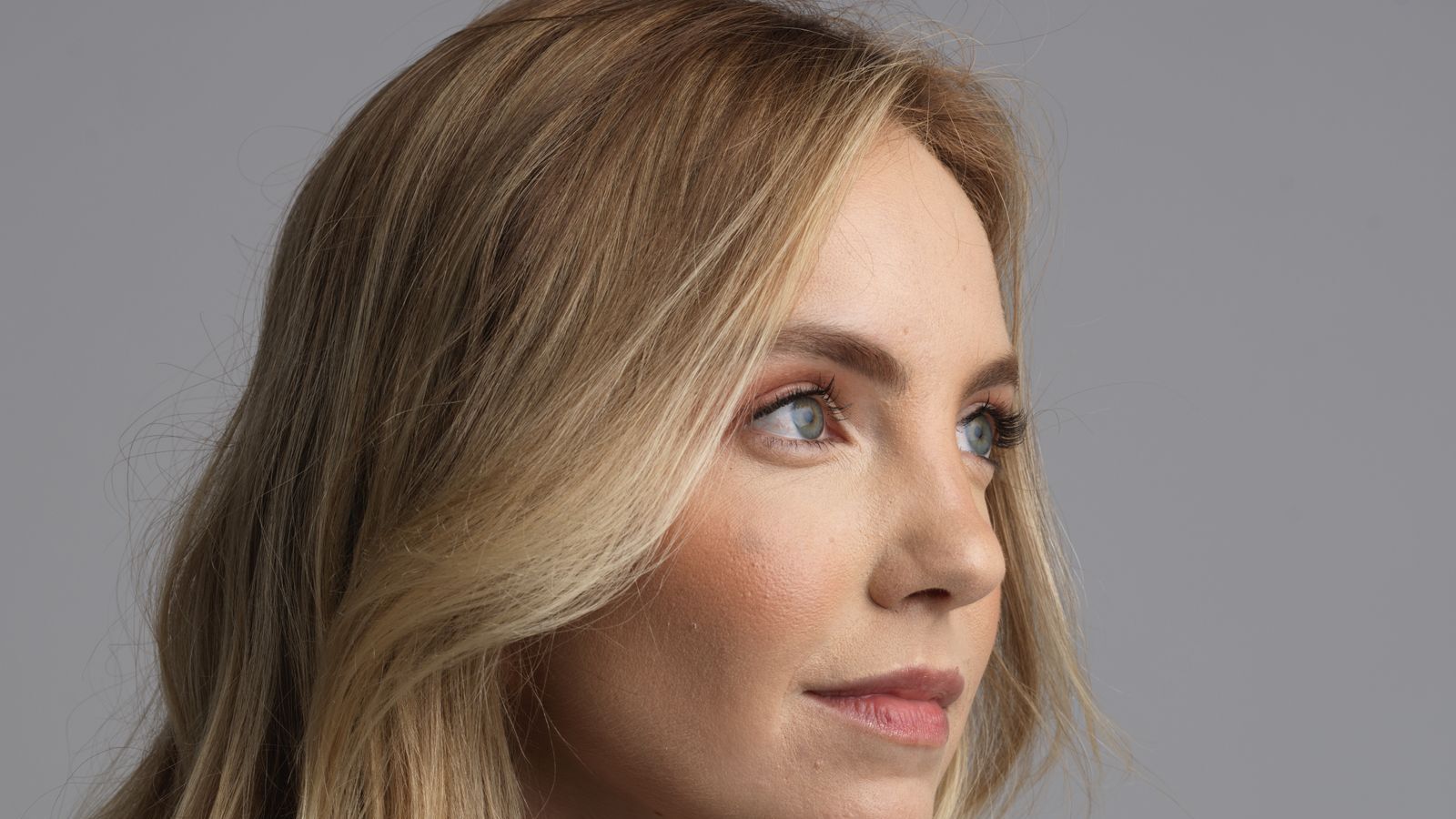 Studio headshot portrait of a woman in profile with soft natural skin tones against a gray backdrop
