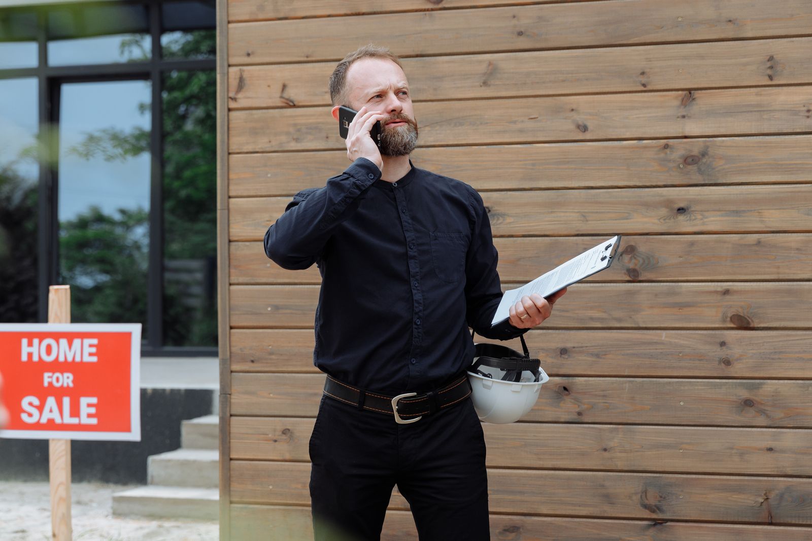 Real estate agent on a phone call outside a house with a for-sale sign