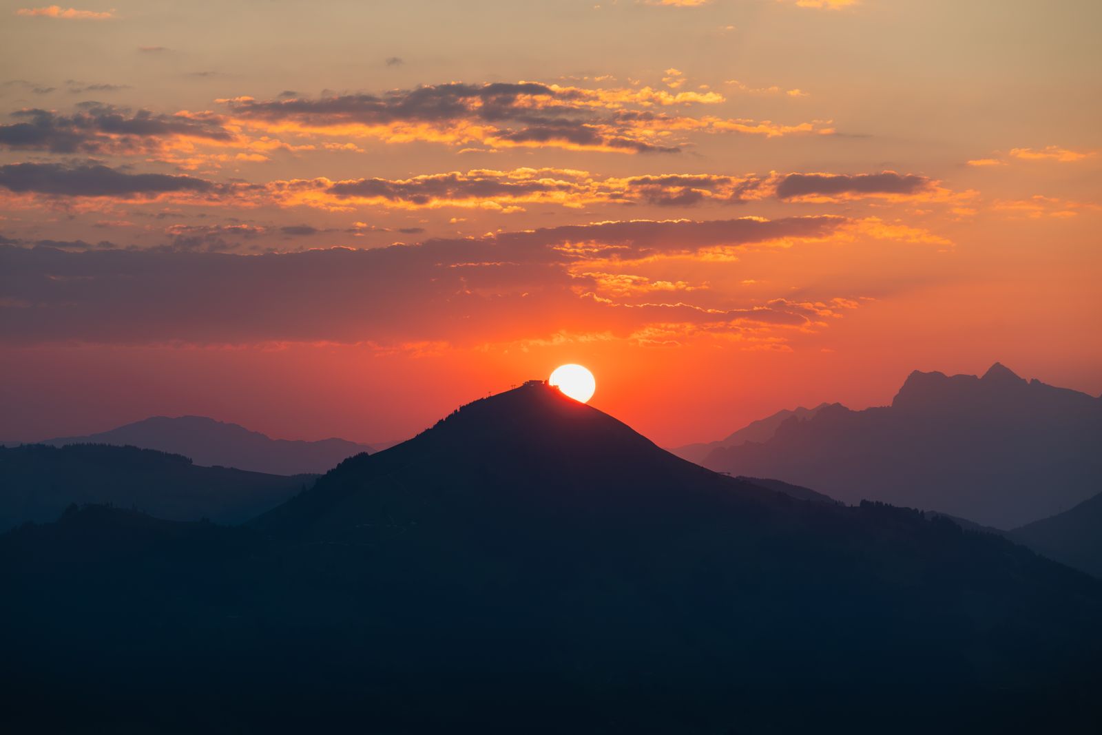Sun cresting a mountain peak at sunrise with an orange and golden sky over layered ridges