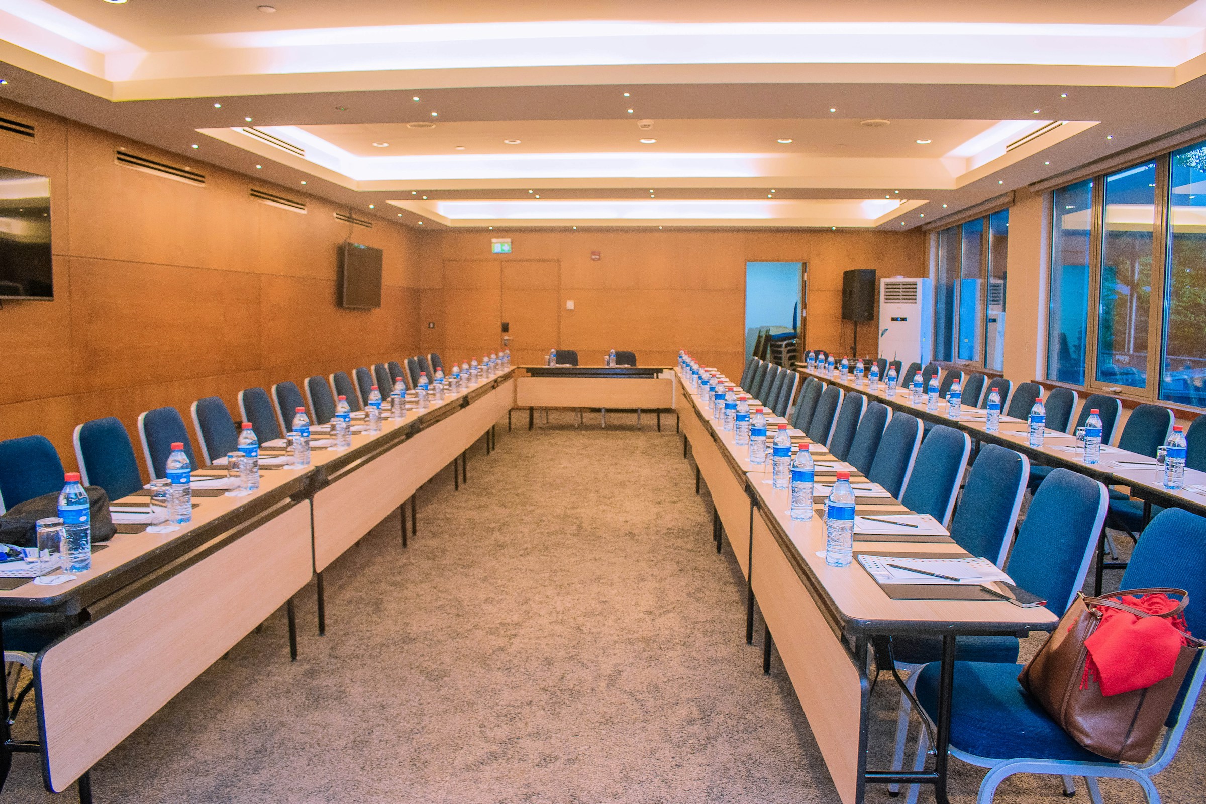 A long empty conference room with narrow tables, blue chairs and bottles of water laid out for a meeting