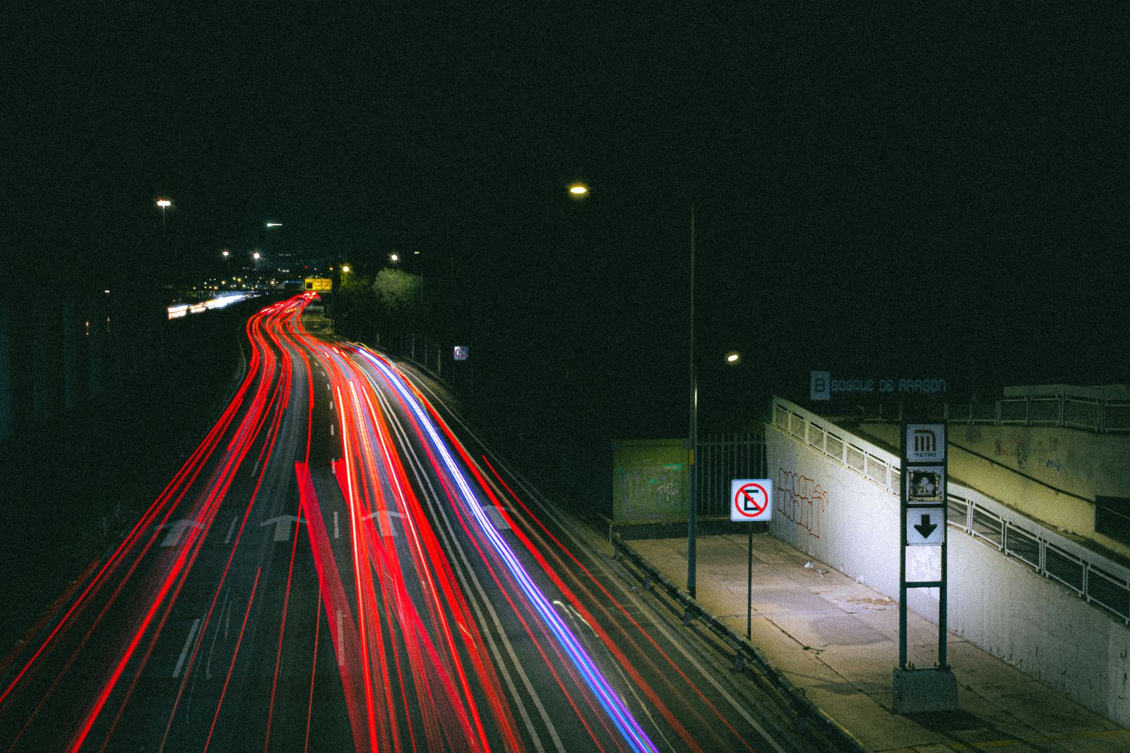 Long exposure of red and blue car light trails curving along a city highway at night