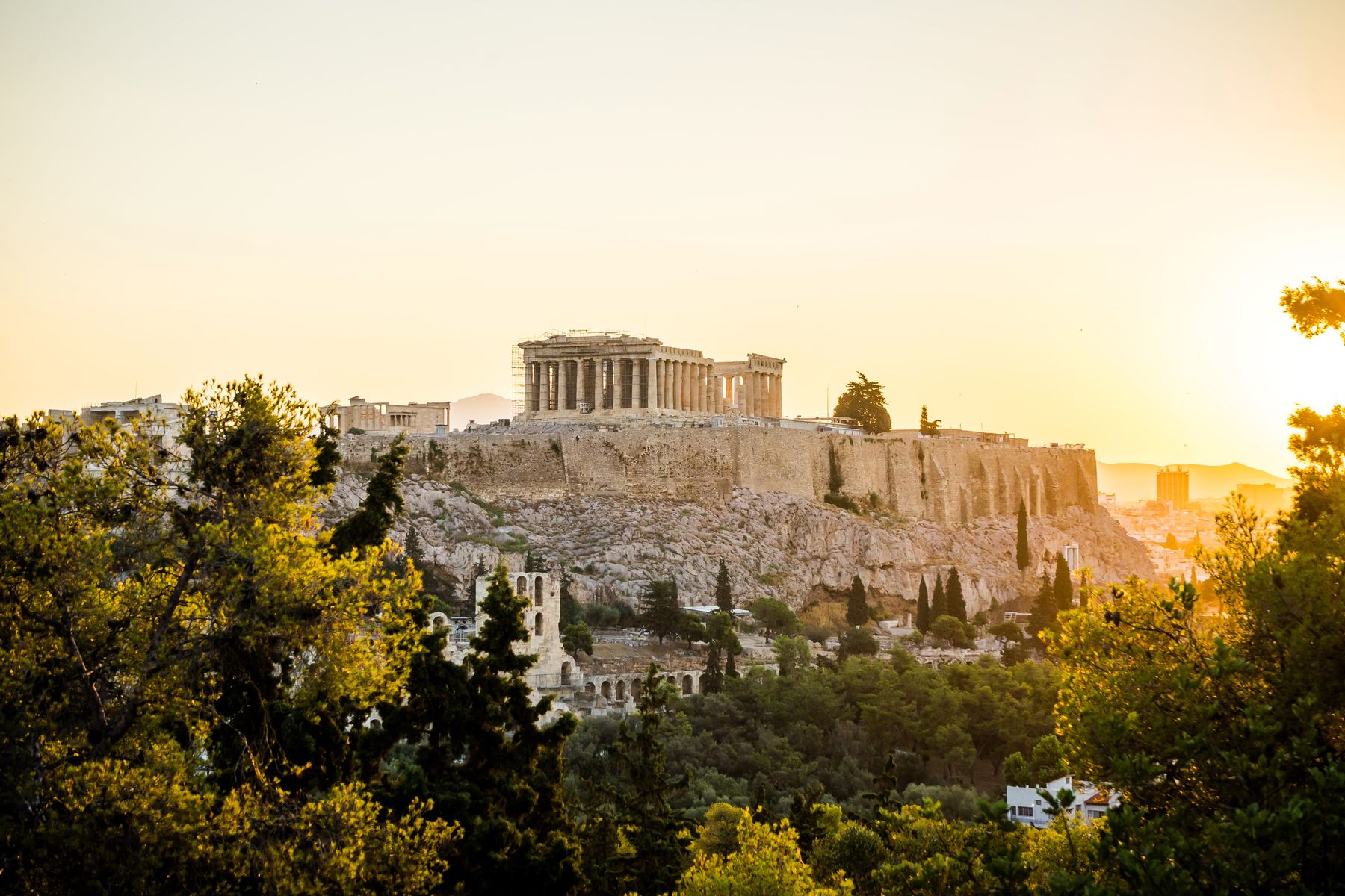 The Acropolis and Parthenon on their rock in warm sunset light seen through trees