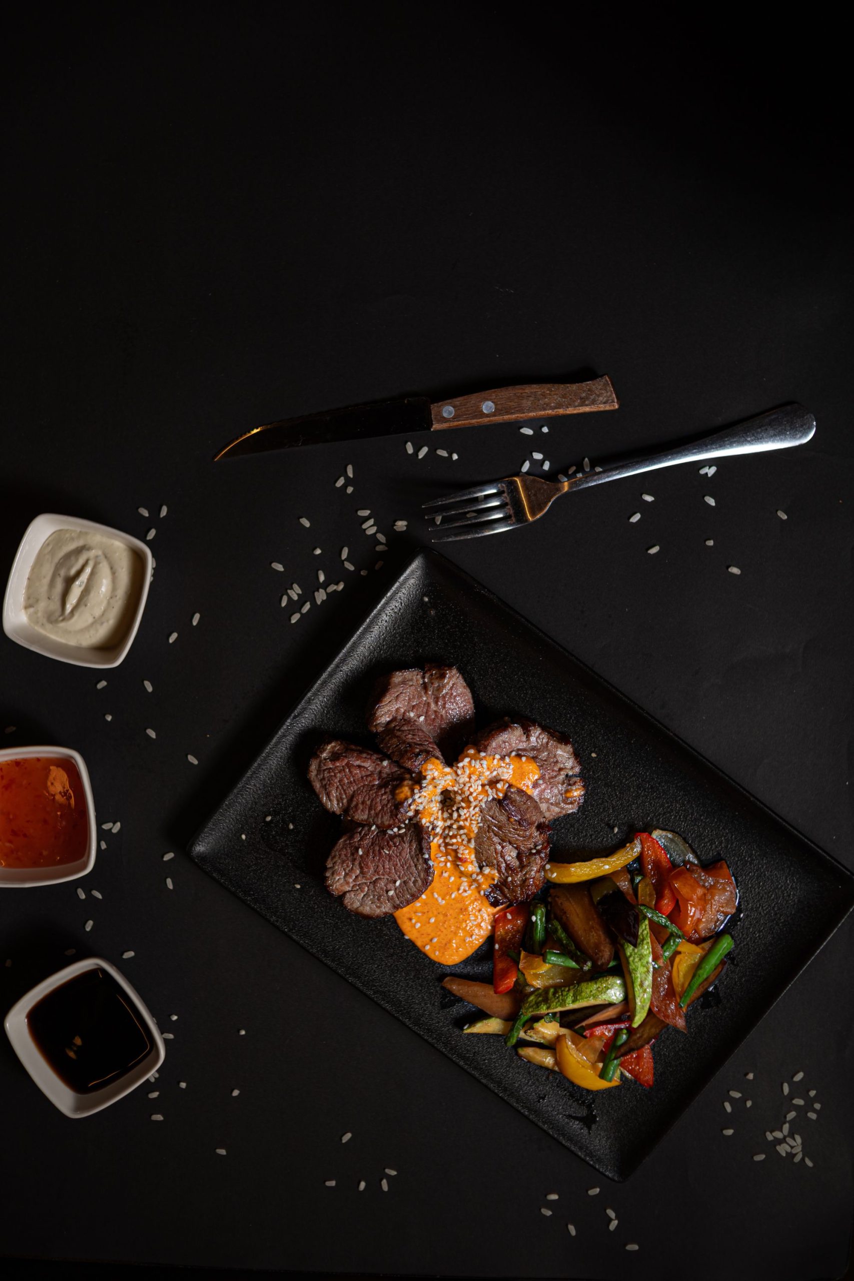 Overhead food photograph of sliced steak and roasted vegetables on a black plate