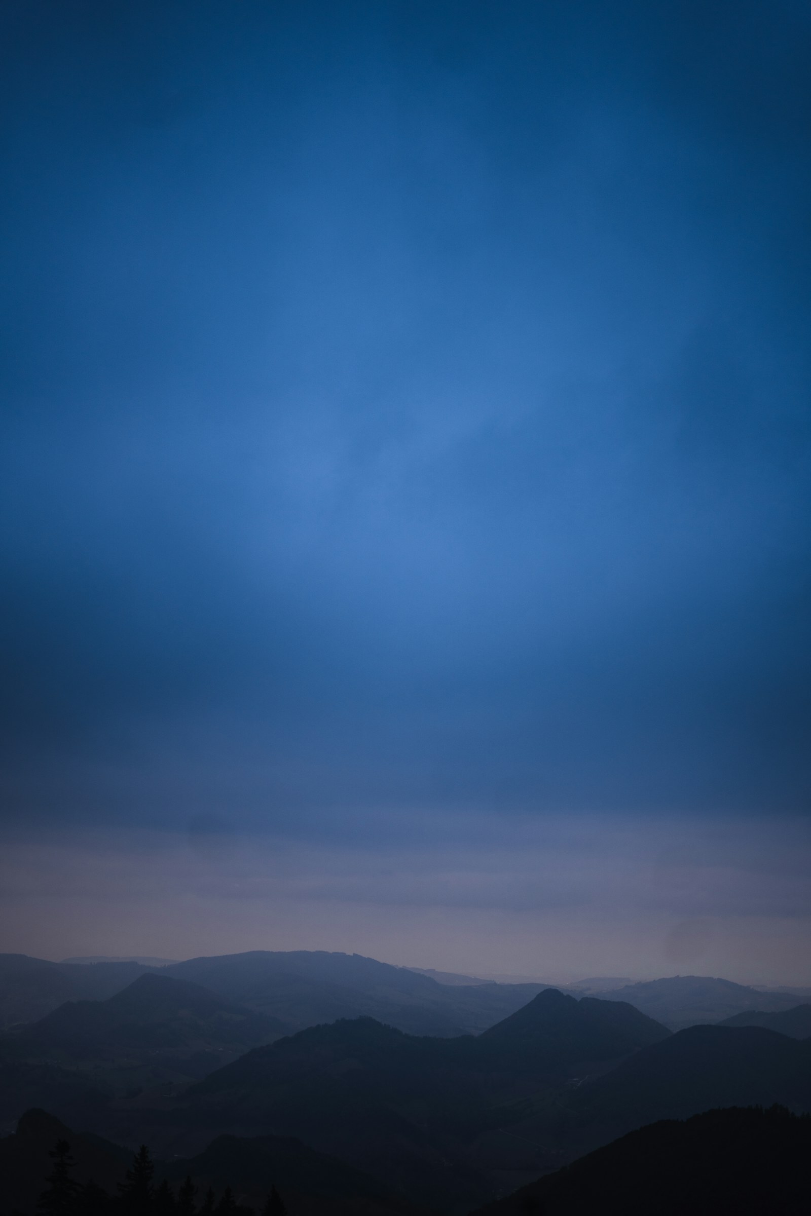 Blue hour sky over layered dark hills and low mist, mountain fog photography