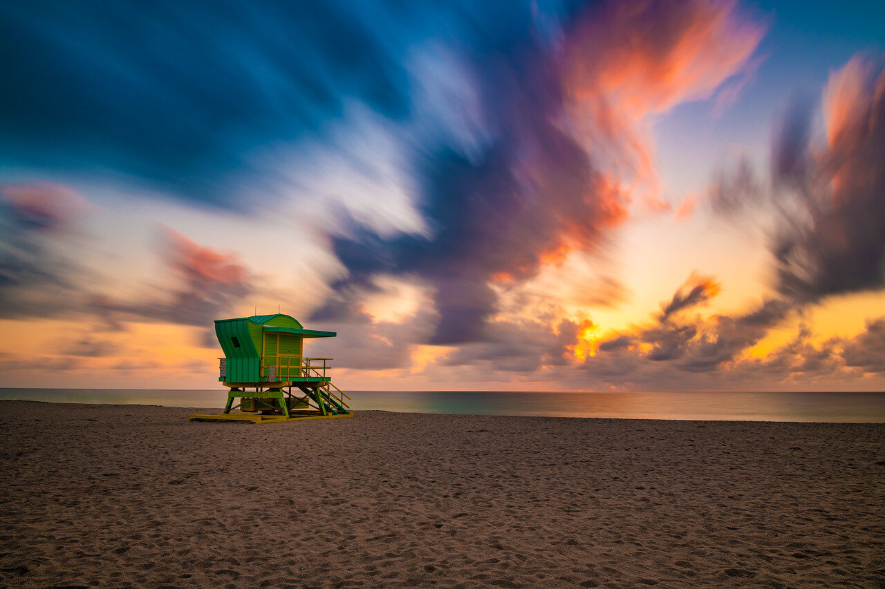 Green lifeguard tower on a Miami beach under streaked blue, purple and orange clouds with warm light near the horizon