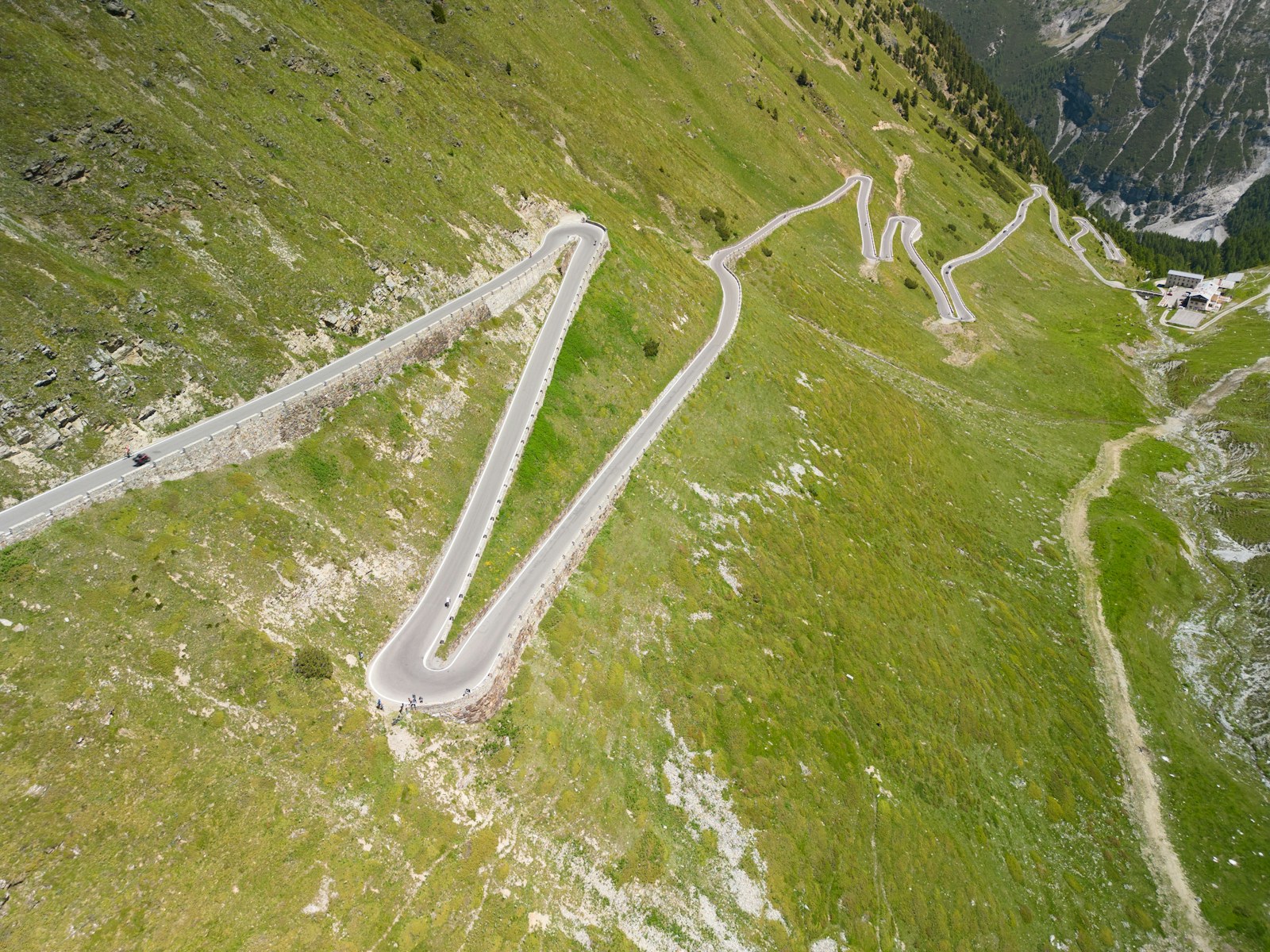 Aerial view of a winding mountain road with tight switchbacks and a few tiny cyclists