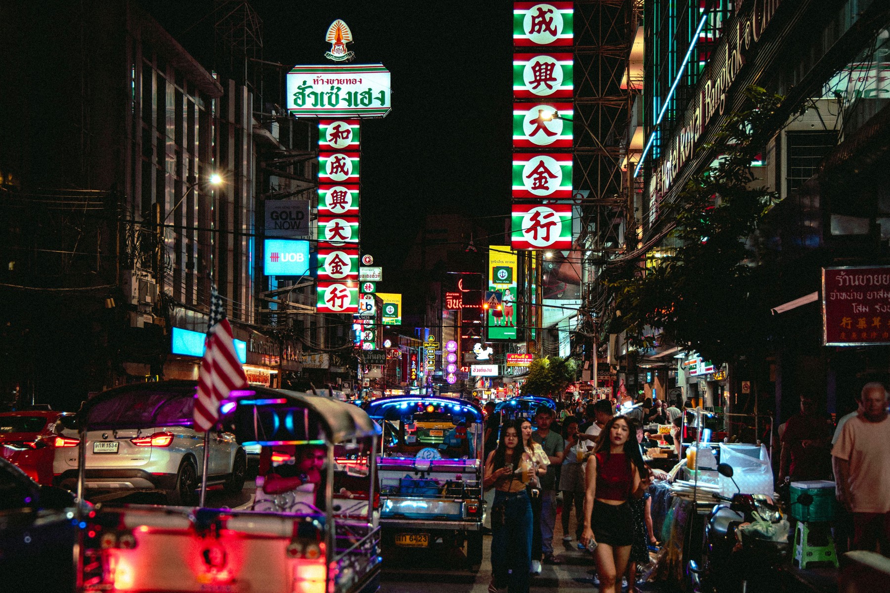 Tuk-tuks and pedestrians beneath neon gold-shop signs on Yaowarat Road in Bangkok at night
