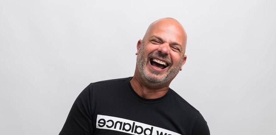 Laughing man in a black shirt against a light gray studio background.