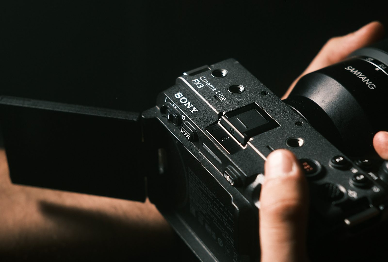 Sony FX3 Cinema Line camera with Samyang lens held in two hands in dark directional light