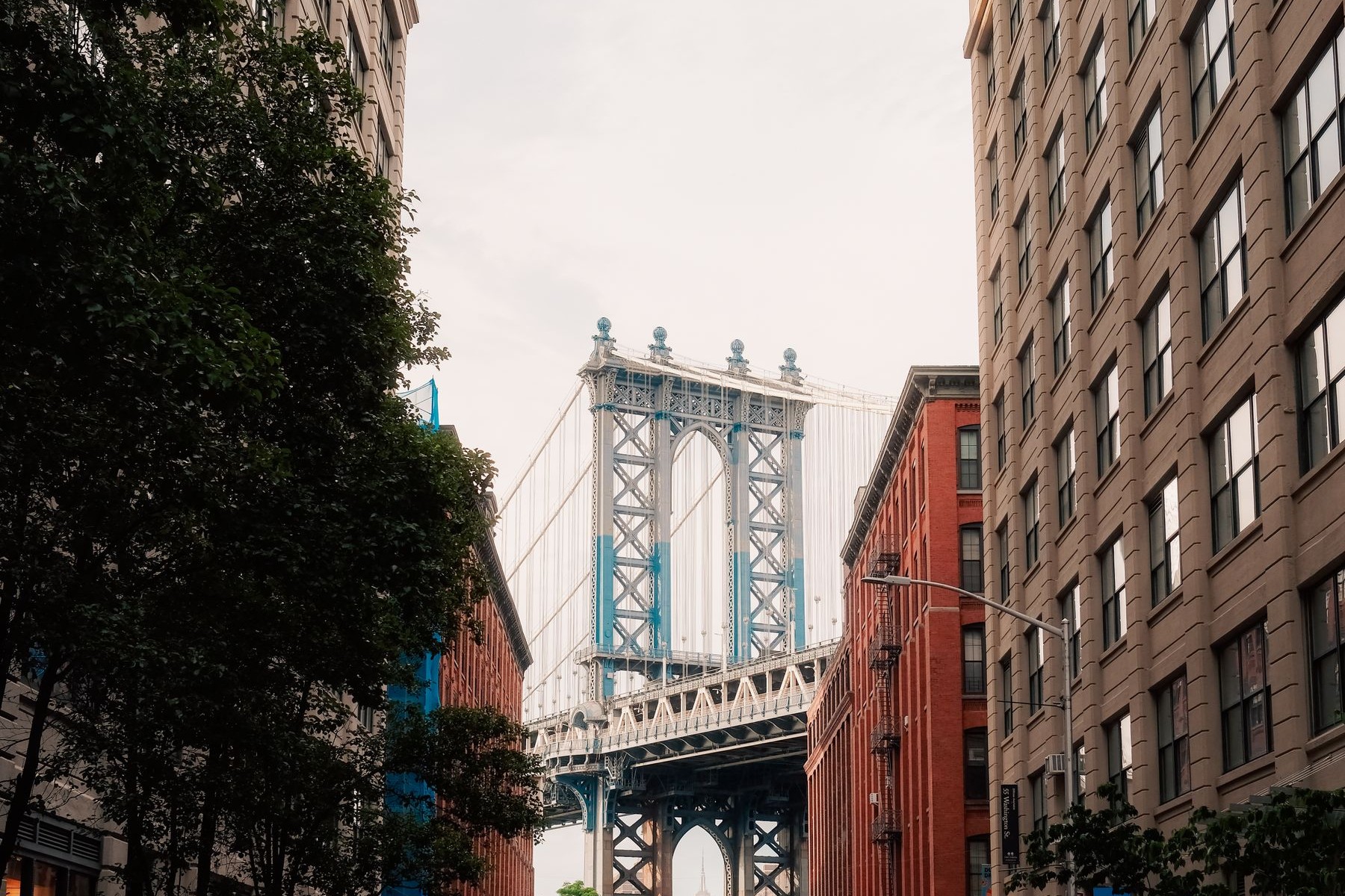 Looking down a brick-paved Brooklyn street in DUMBO toward the Manhattan Bridge tower framed between a red brick building and a tall tan warehouse