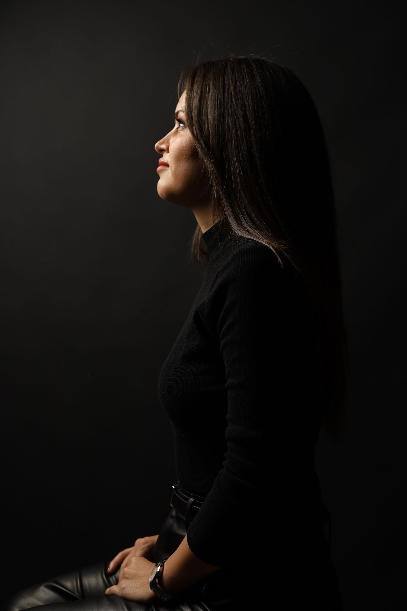 Woman in black seen in profile against a dark background, lit from the side