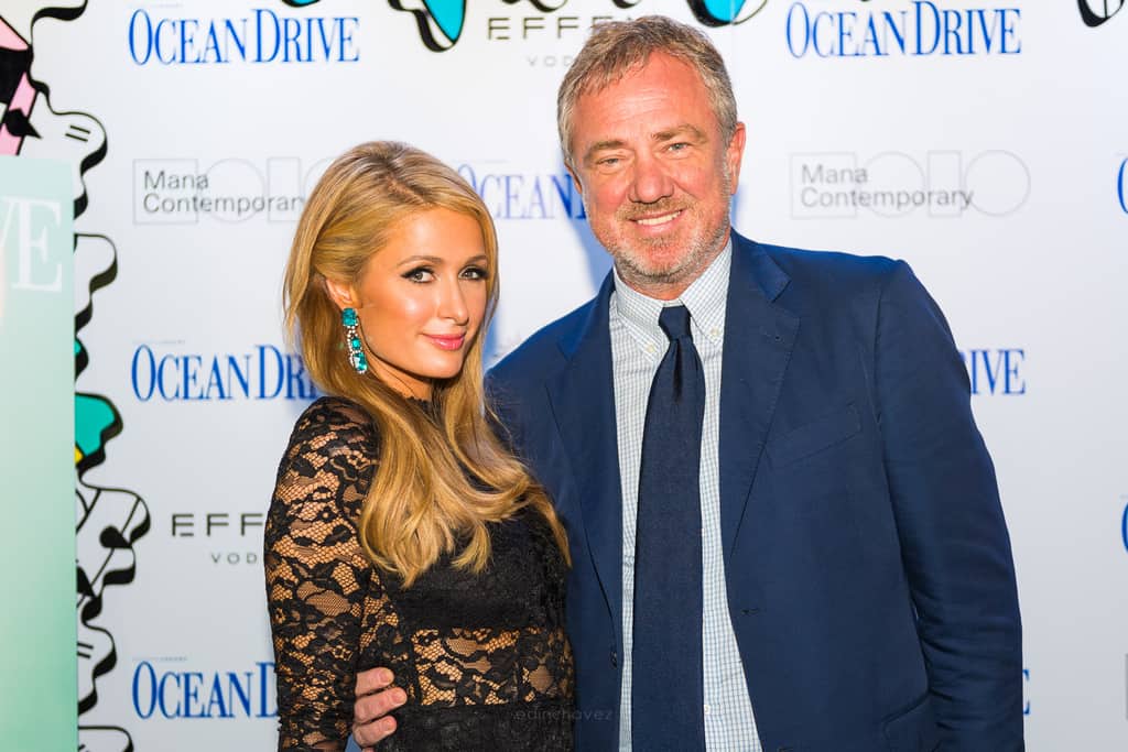 Two guests posing at a red-carpet event in front of a sponsor backdrop