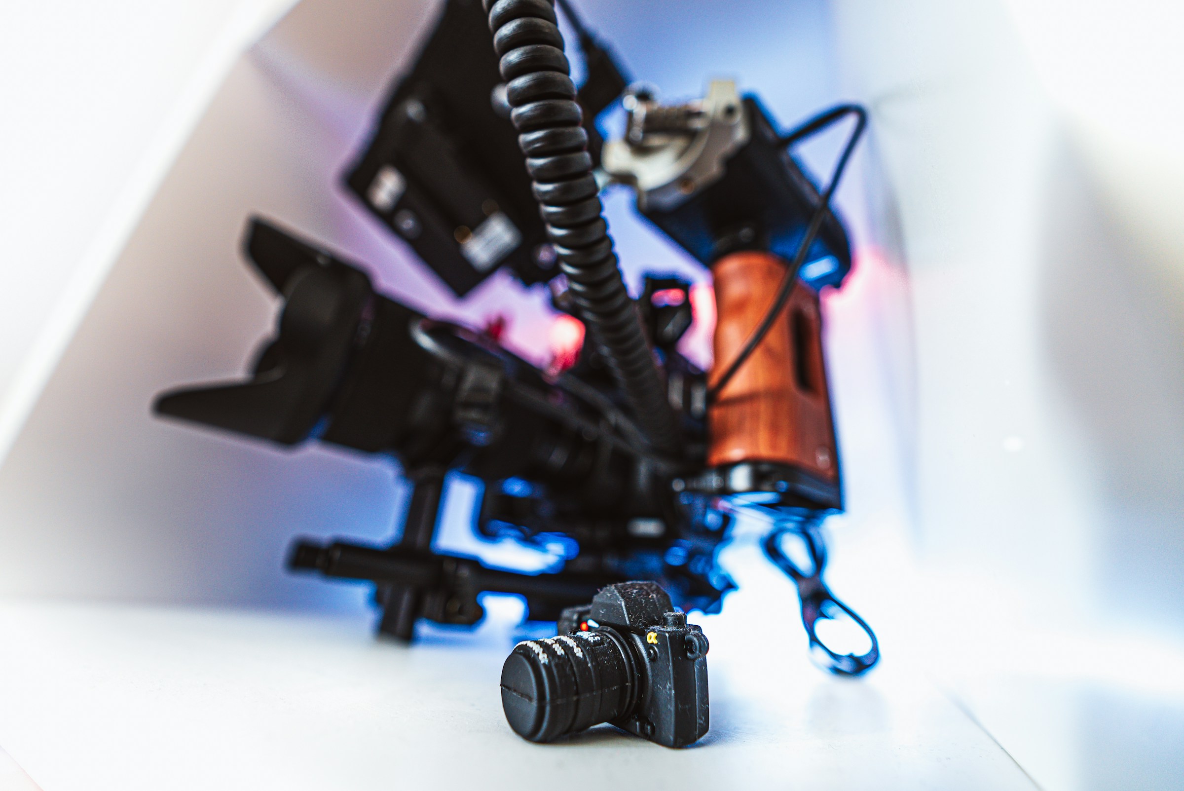 A camera rig with a cage, handle and cable next to a small camera on a white surface