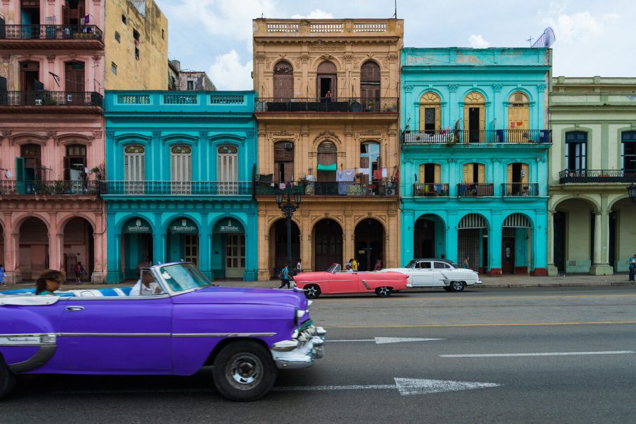 Purple vintage convertible passes teal and pastel buildings on a Havana street