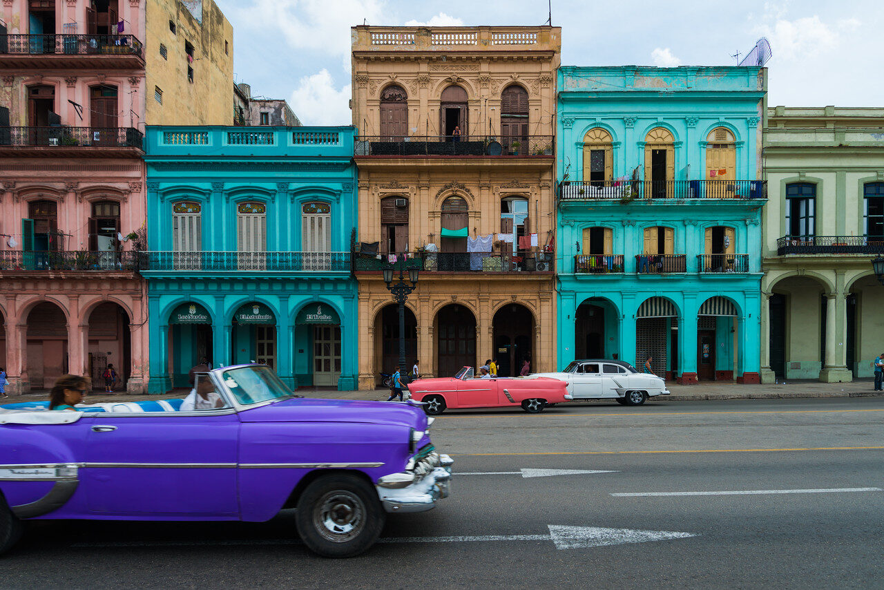 Purple vintage convertible passes teal and pastel buildings on a Havana street