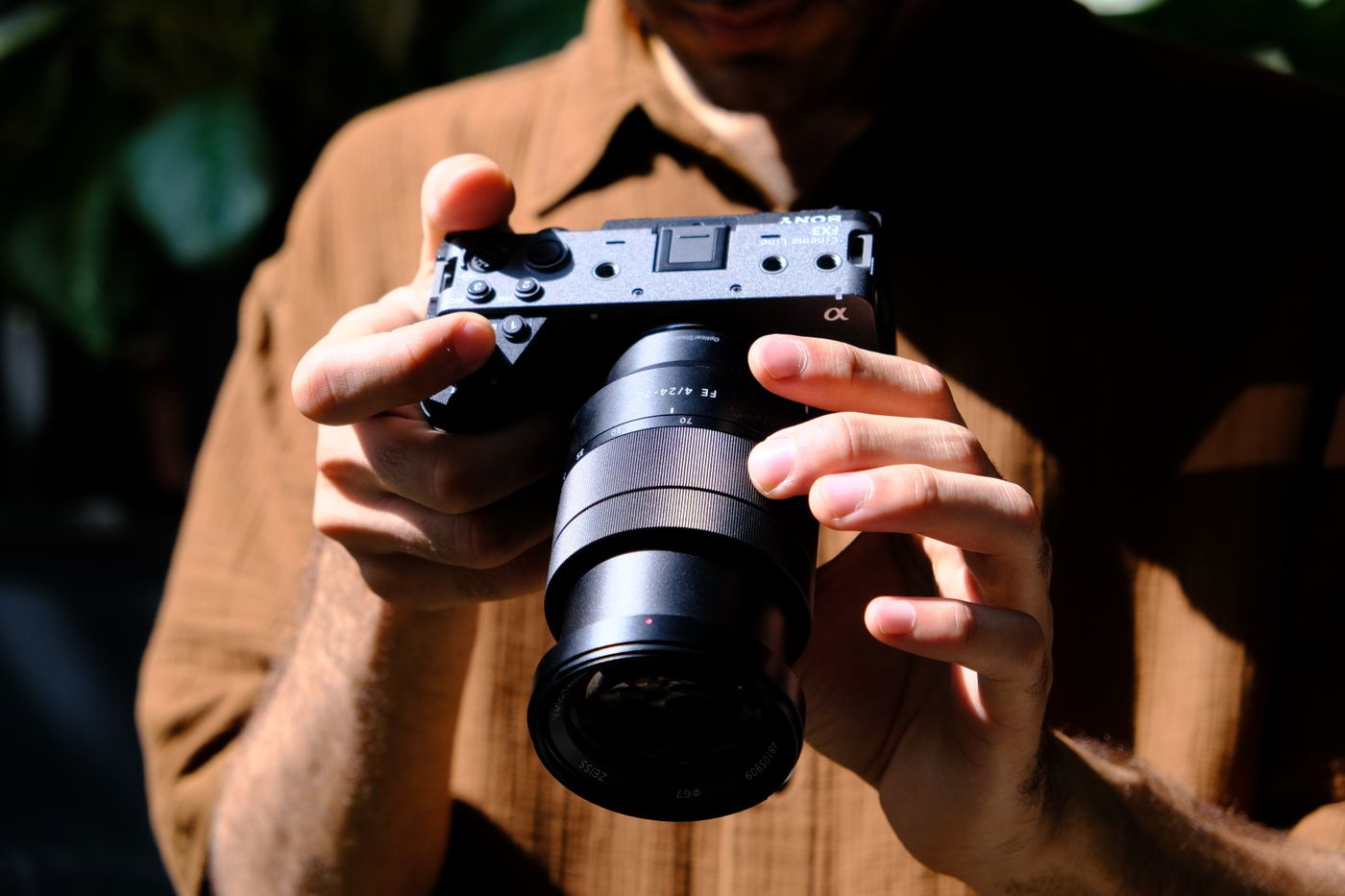 A person holding a mirrorless camera with a lens in both hands outdoors.