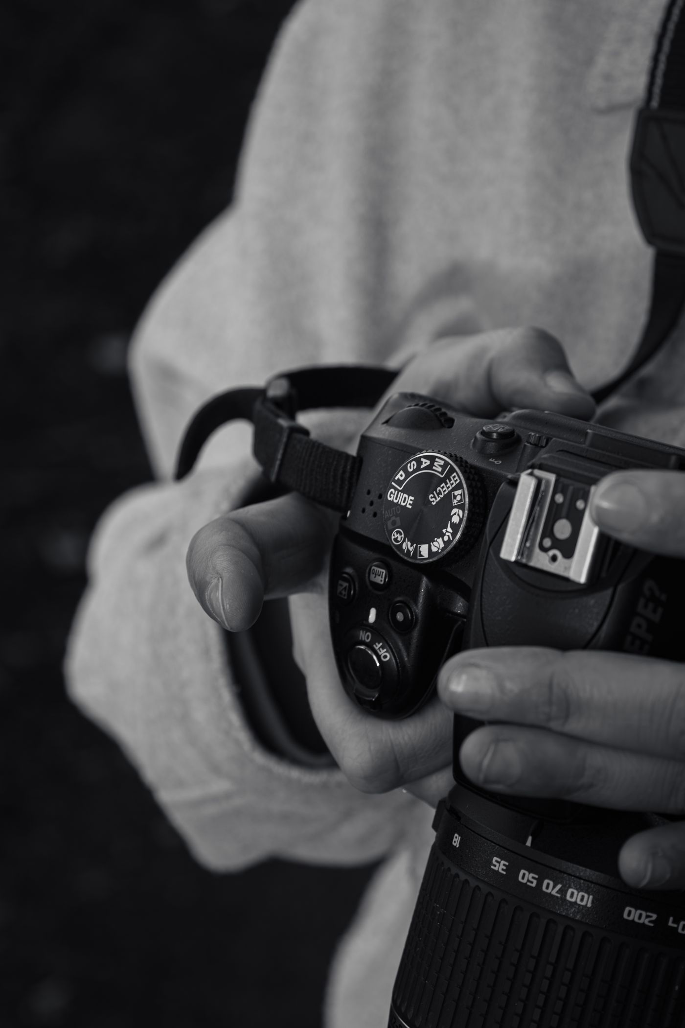 Black and white photo of hands adjusting a camera's settings dial.