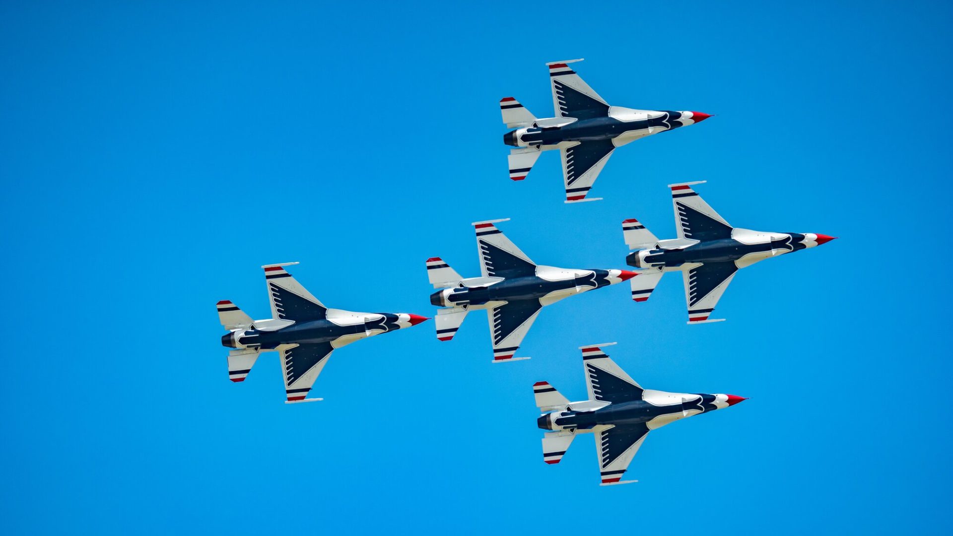 Five jets in a tight formation against a clear blue sky at an air show