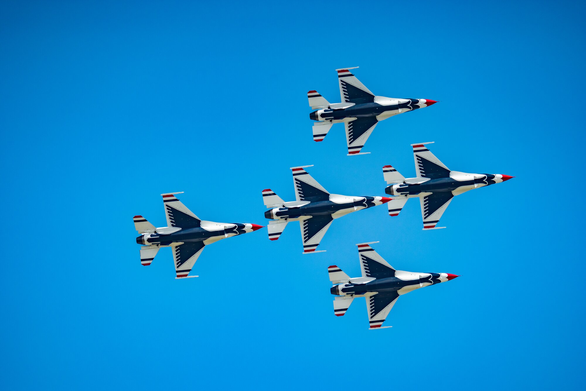 Five jets in a tight formation against a clear blue sky at an air show