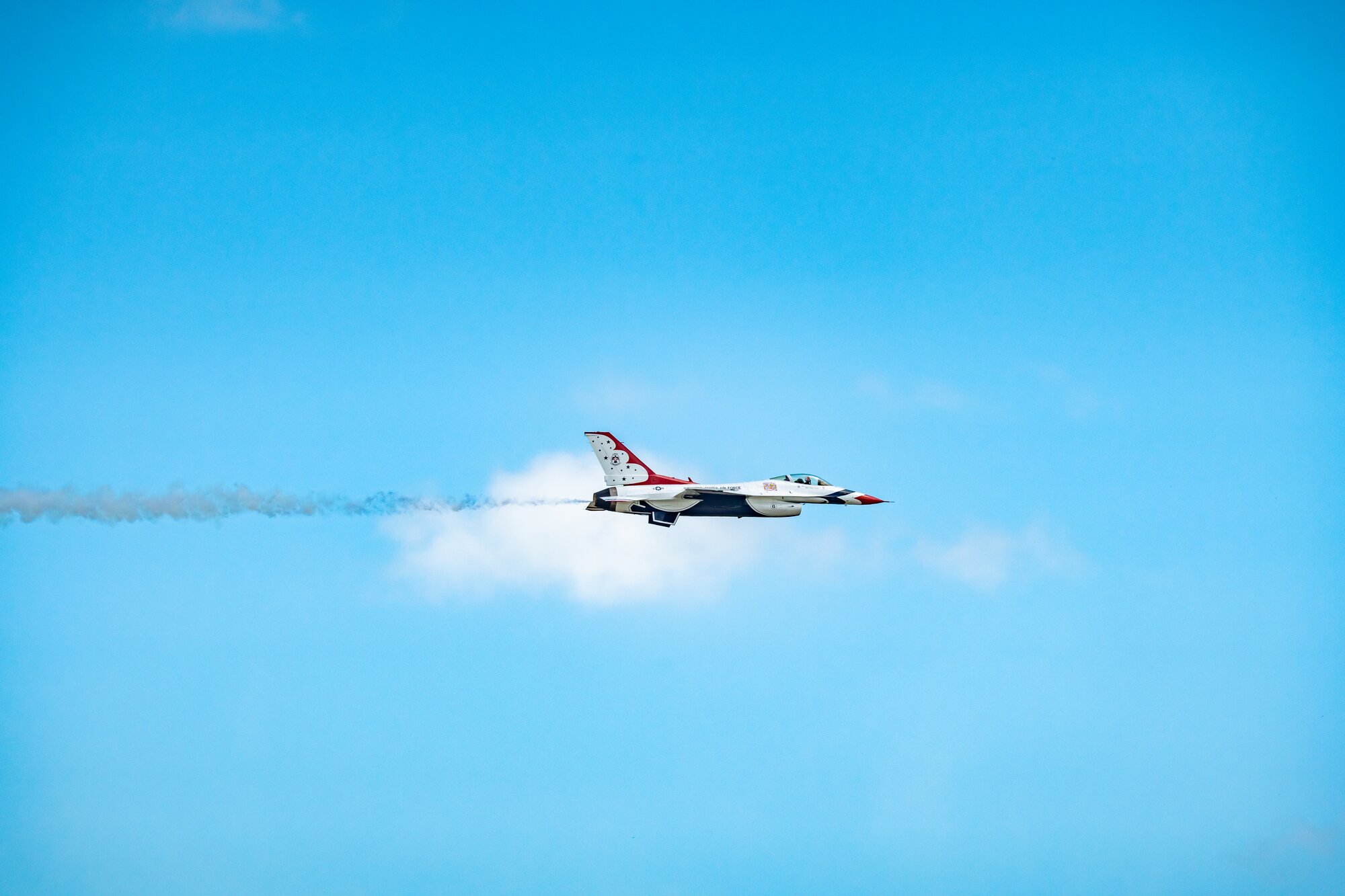 A single jet with a short smoke trail flying left to right across a clear blue sky