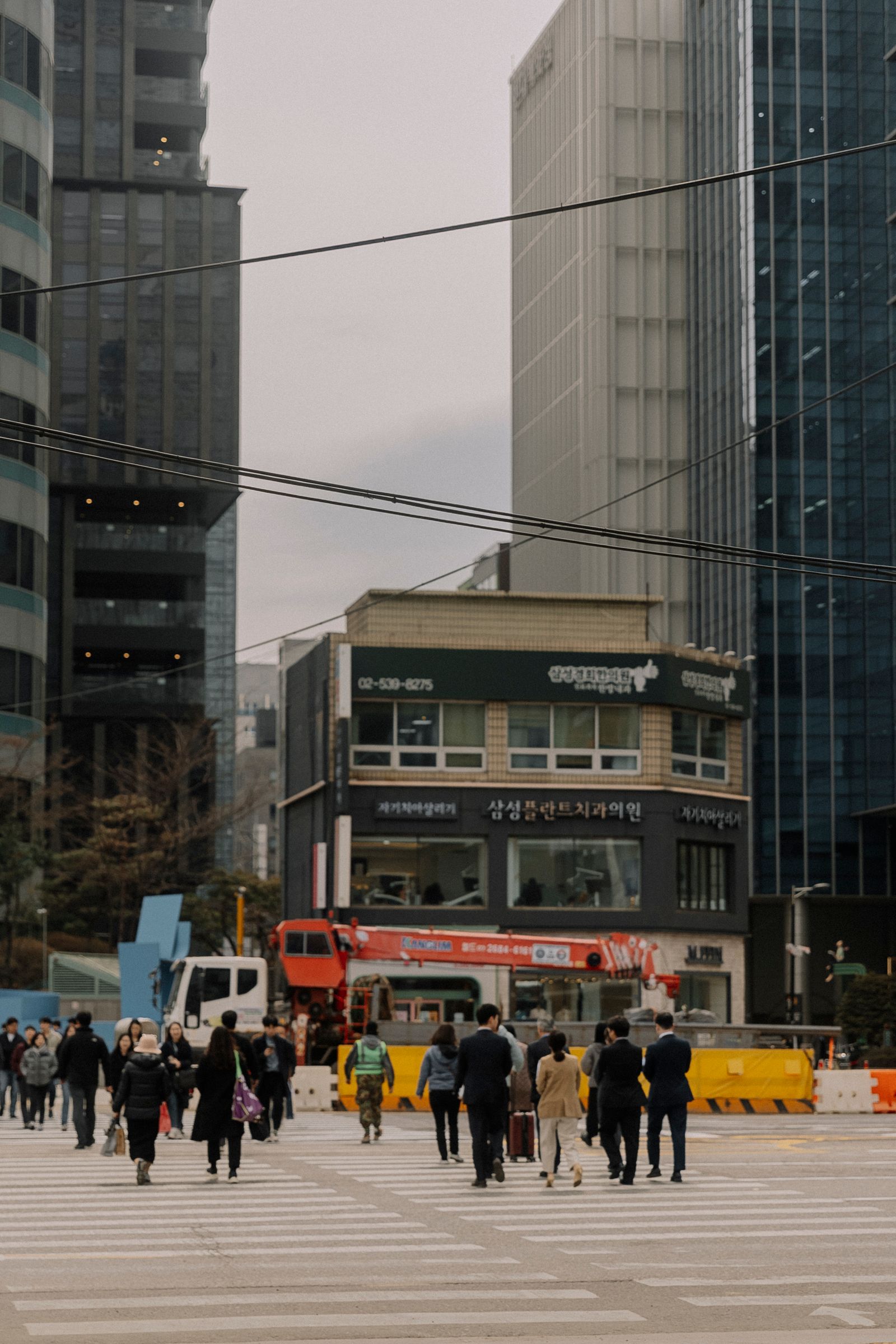 Pedestrians at a crosswalk below city towers and a bus
