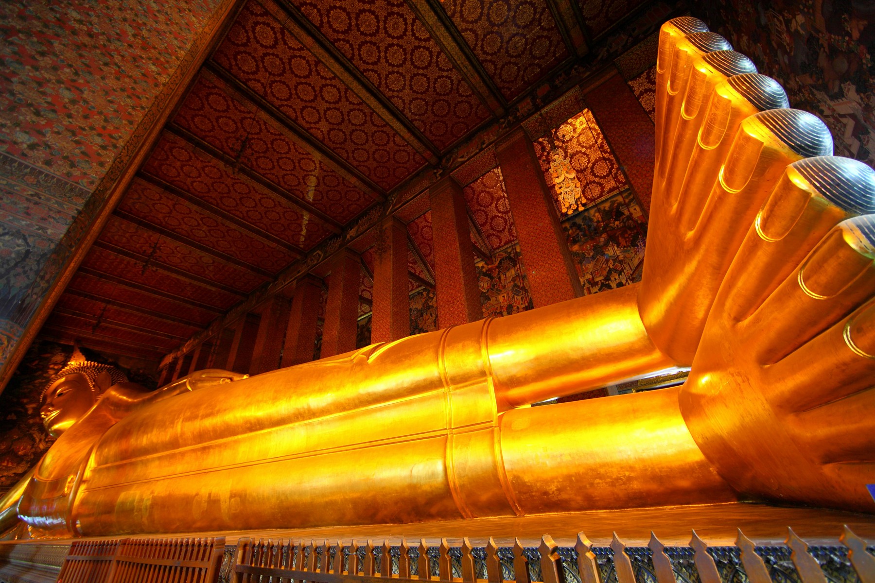 Golden reclining Buddha beneath the patterned ceiling inside Wat Pho in Bangkok