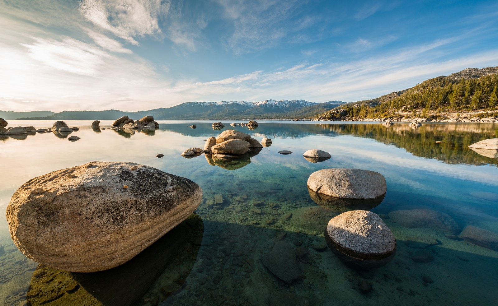 Granite boulders in clear Lake Tahoe water under a blue sky with wispy clouds