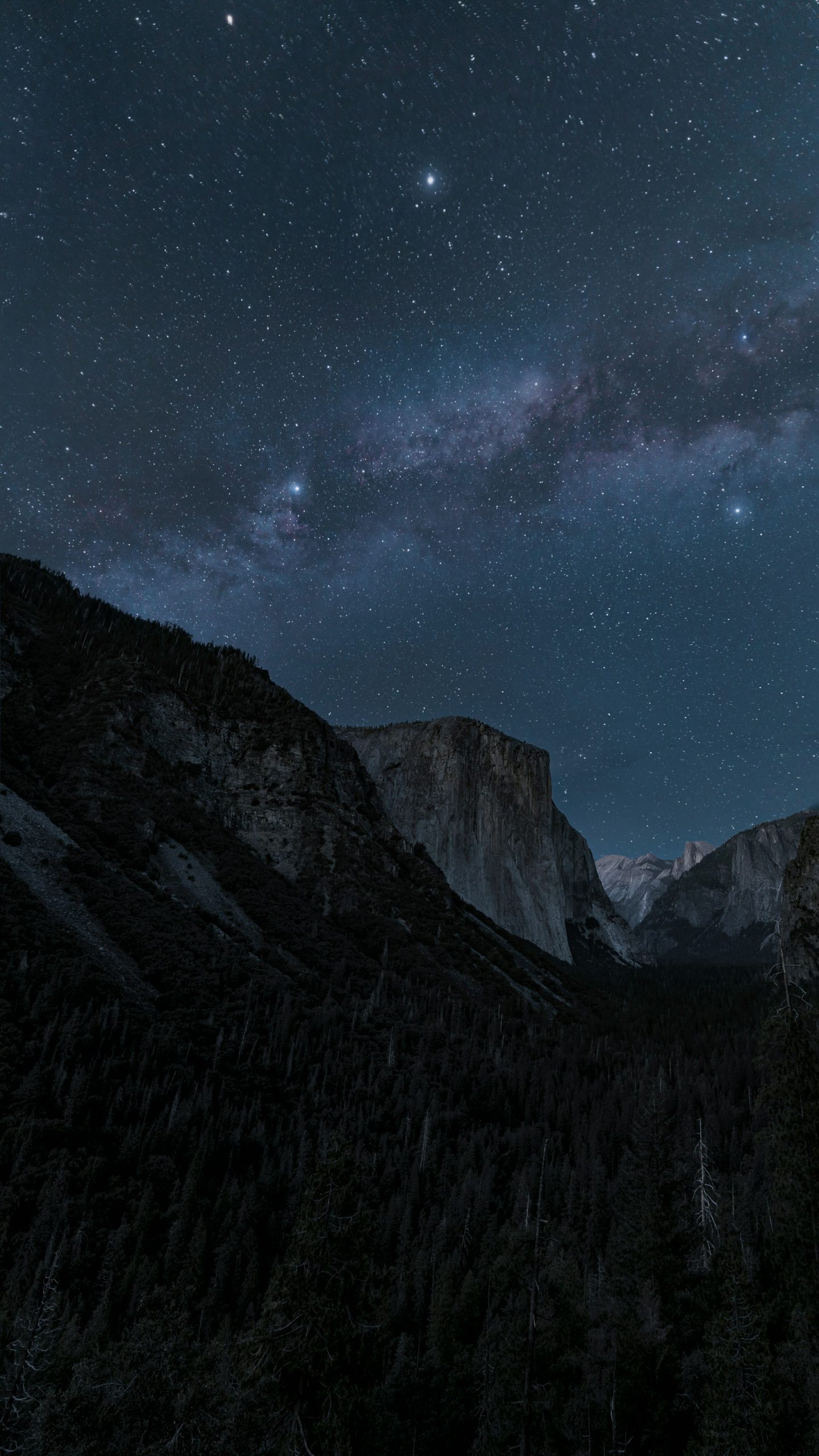 Milky Way and stars above the granite cliffs and forests of Yosemite Valley at night