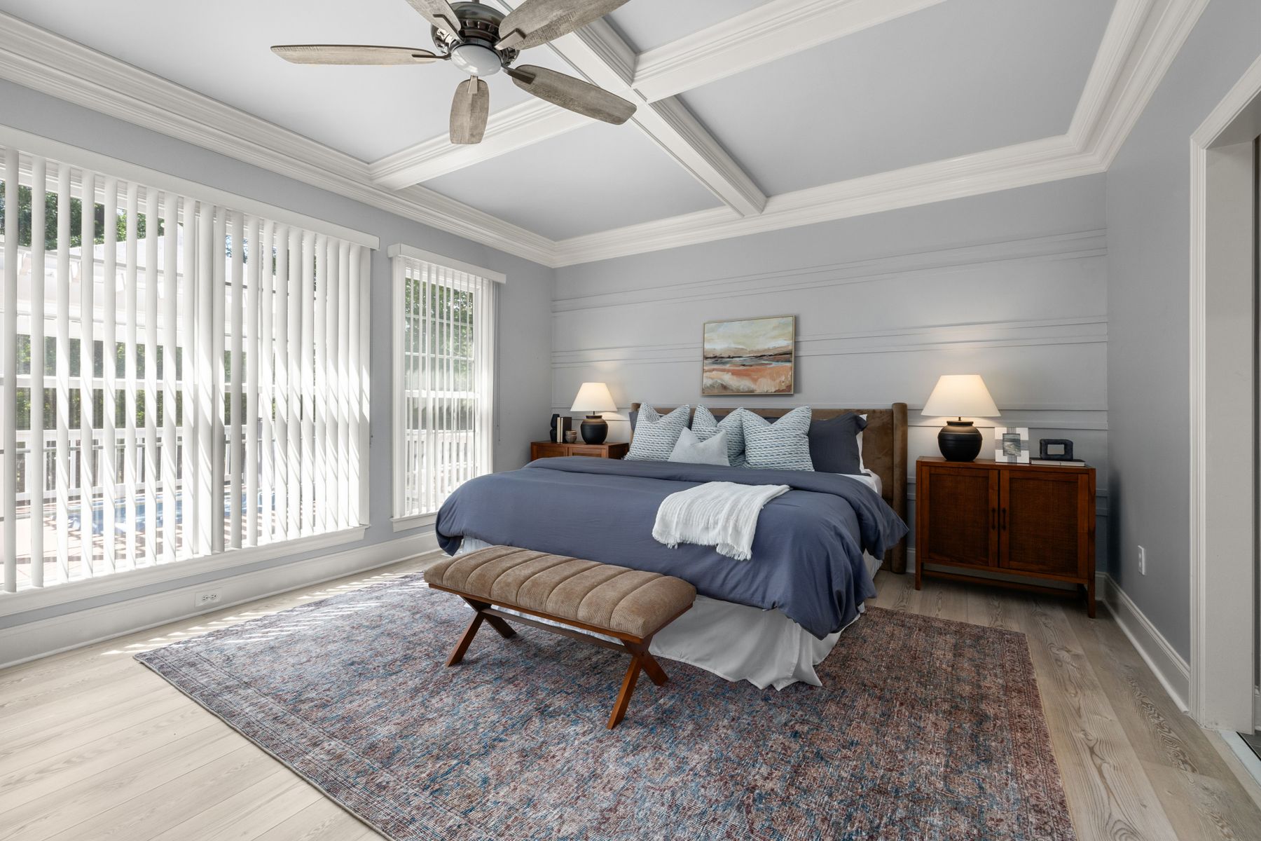 Bright primary bedroom with a neatly made bed and soft daylight from large windows.
