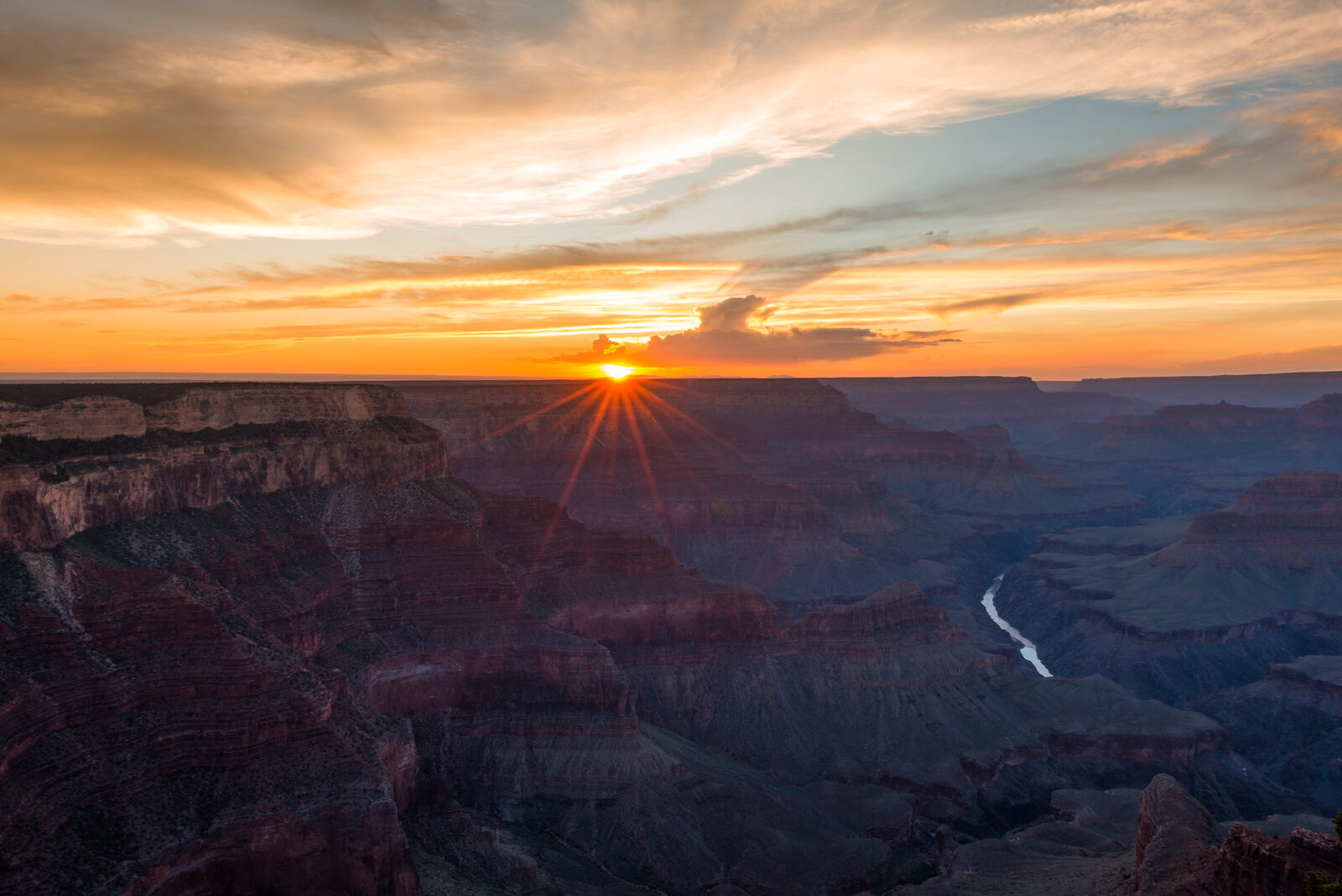 Sunset over the Grand Canyon with a starburst sun, orange clouds and layered red rock walls