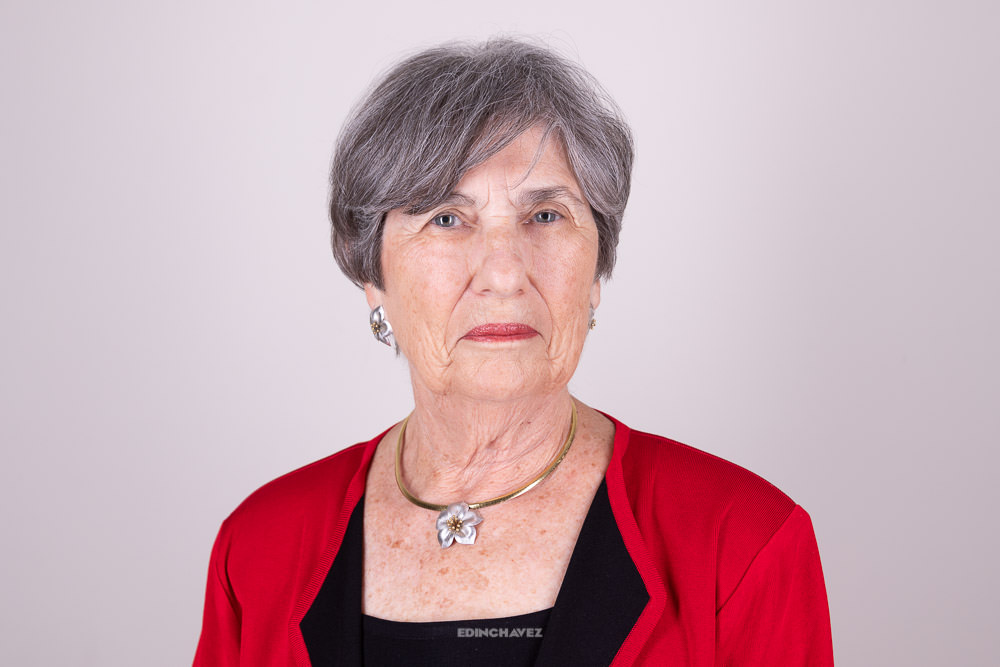 Studio headshot of a woman with short gray hair in a red jacket against a plain light background