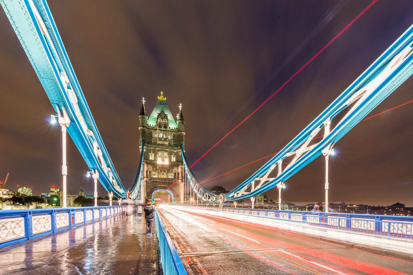 Tower Bridge at night with blue lit railings, light trails on the road and wet pavement reflecting the lights