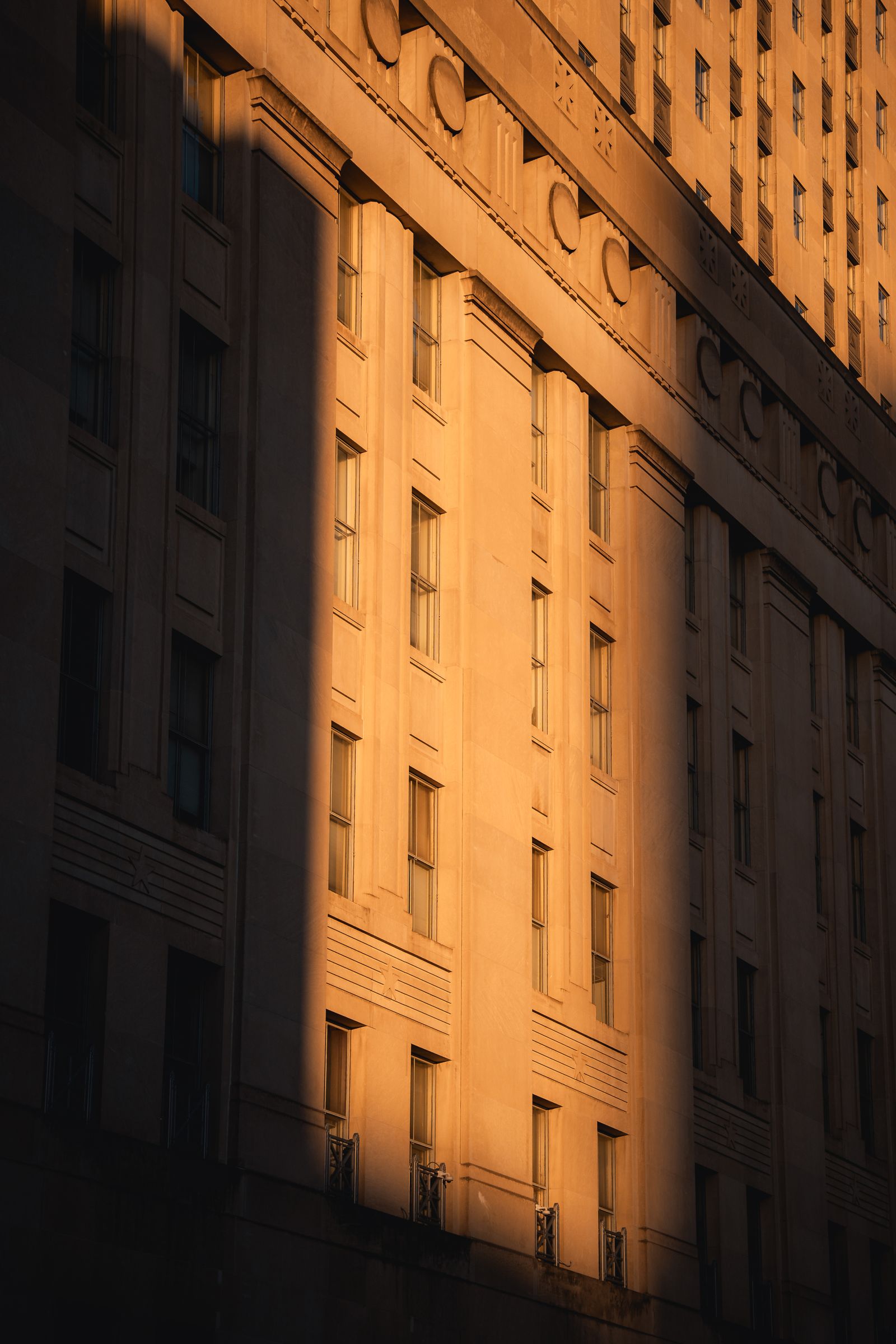 Warm golden light falling across the stone facade of a tall building with deep shadow on one side
