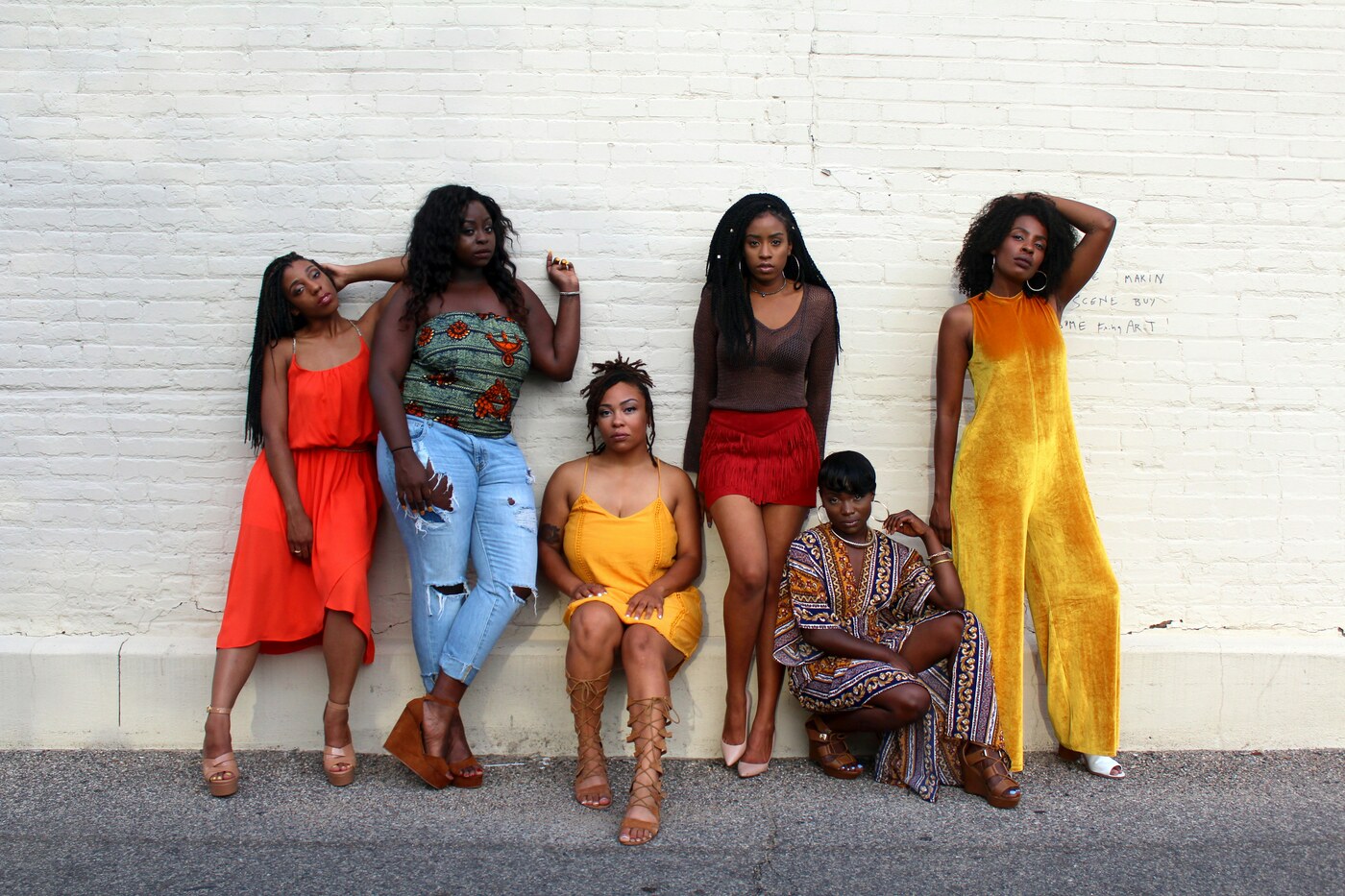 Six people pose along a white brick wall in daylight