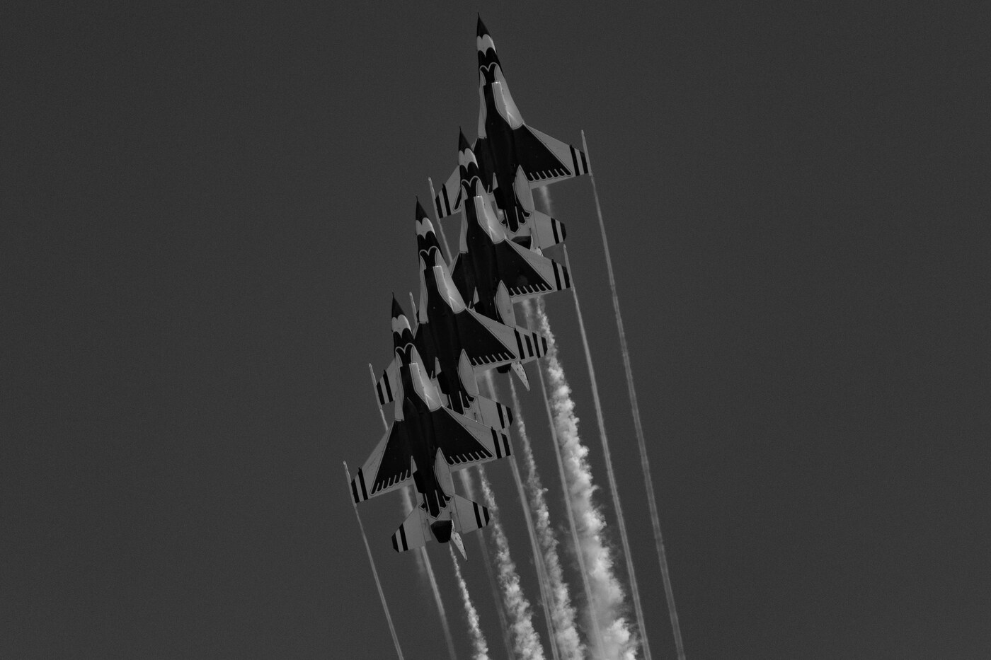 Black and white photo of a stack of USAF Thunderbirds F-16 jets climbing steeply with parallel smoke trails