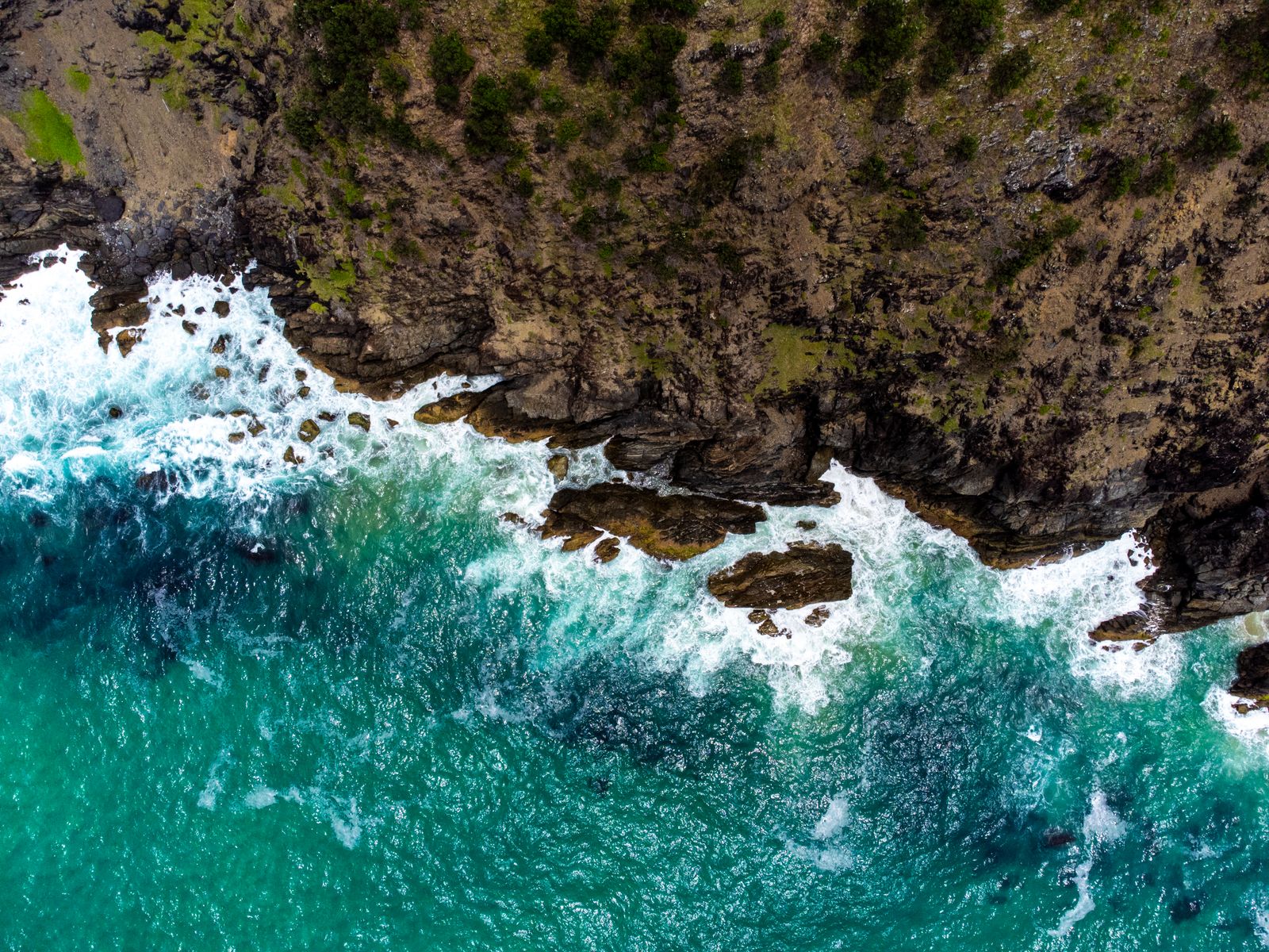 Top-down aerial view of turquoise waves breaking against a rocky brown shoreline