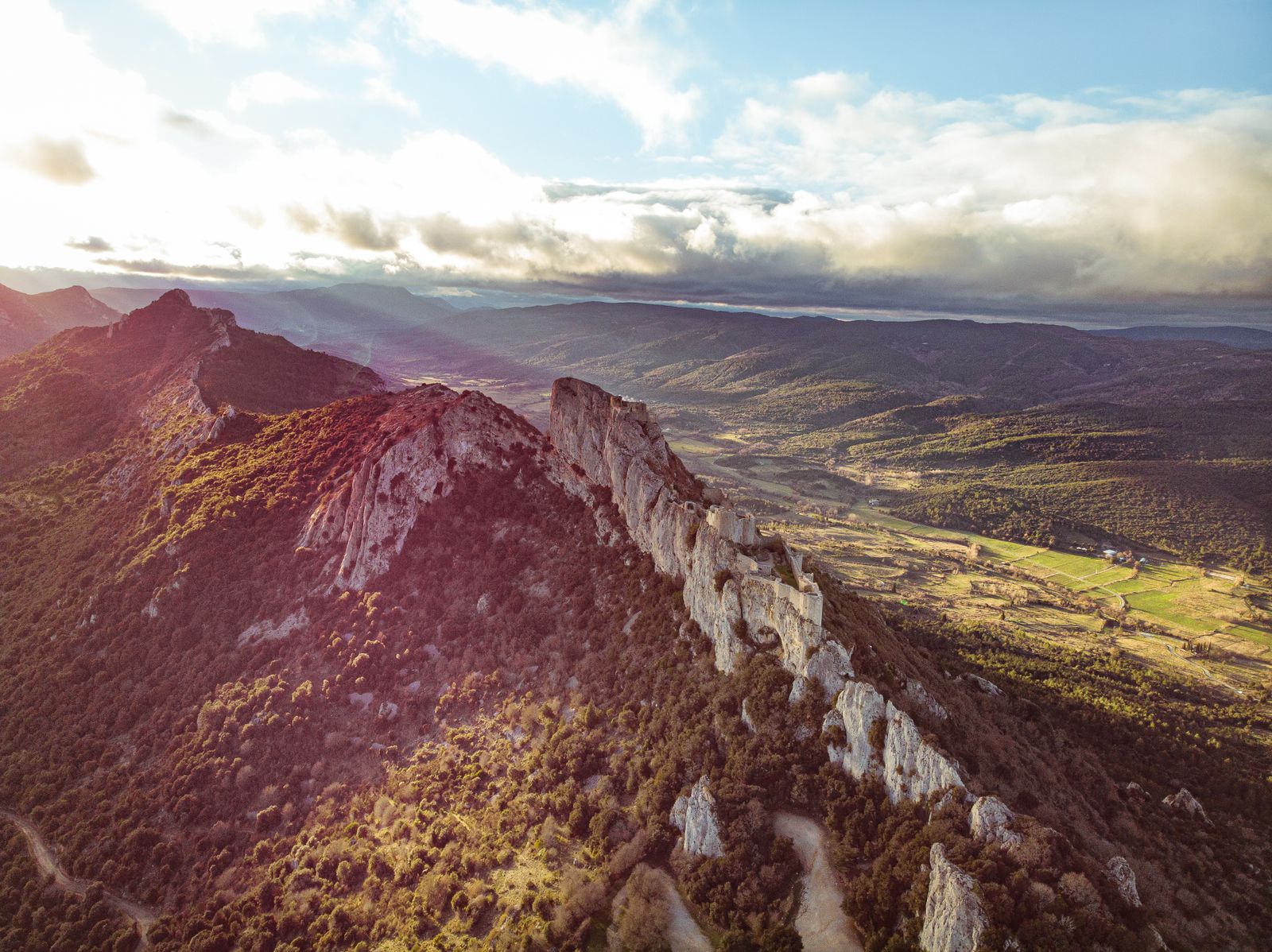 Aerial view of a rugged mountain ridge and green valley under a bright morning sky with clouds