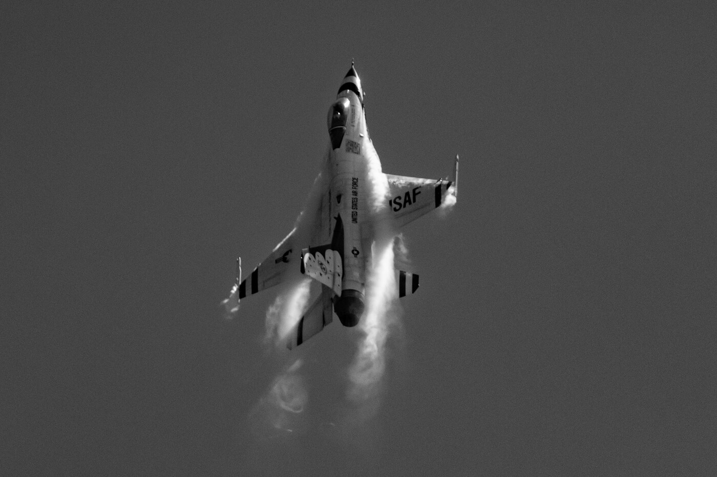 Black and white photo of a USAF Thunderbirds F-16 pulling steeply upward with vapor off the wings