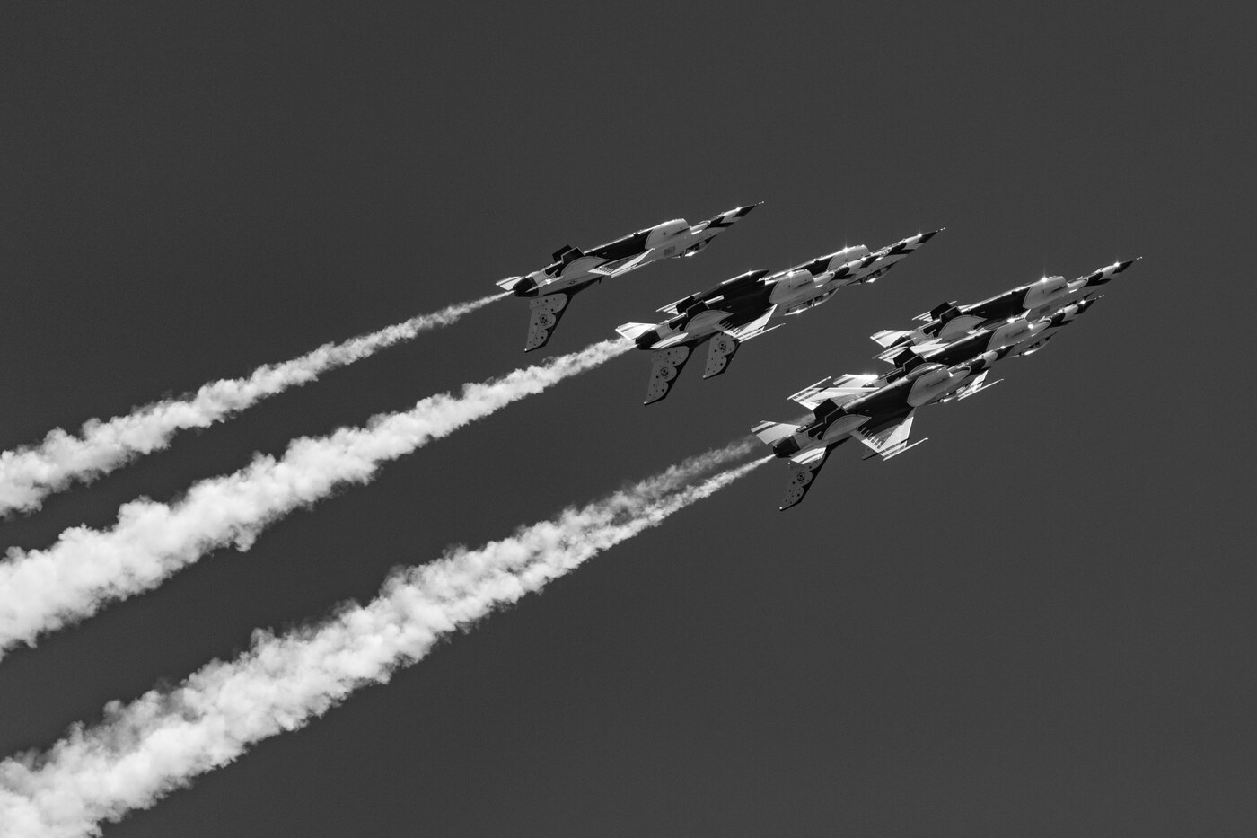 Black and white photo of four USAF Thunderbirds F-16 jets in a diagonal formation with long parallel smoke trails