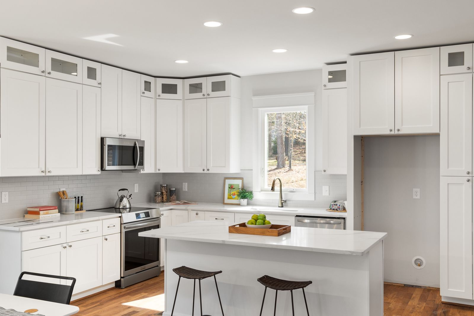 Bright white kitchen with an island, shaker cabinets, stainless steel appliances and a window, an interior real estate photography example